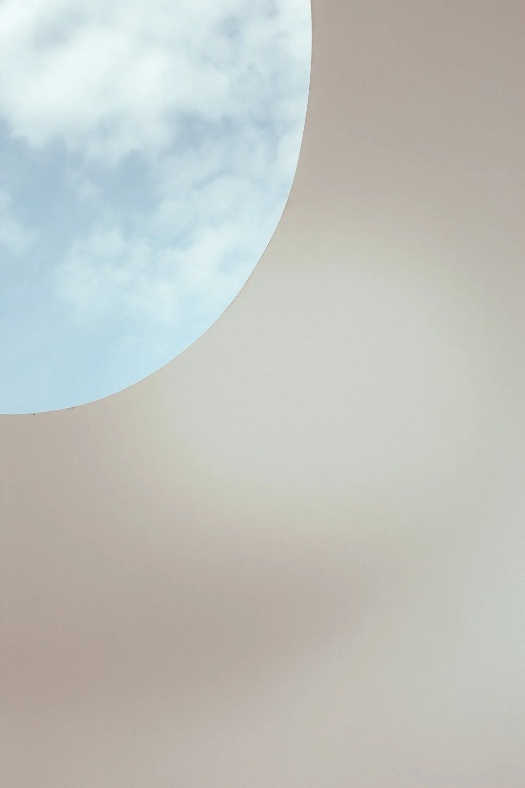 A view of blue sky with some clouds through a circular opening in a beige surface.