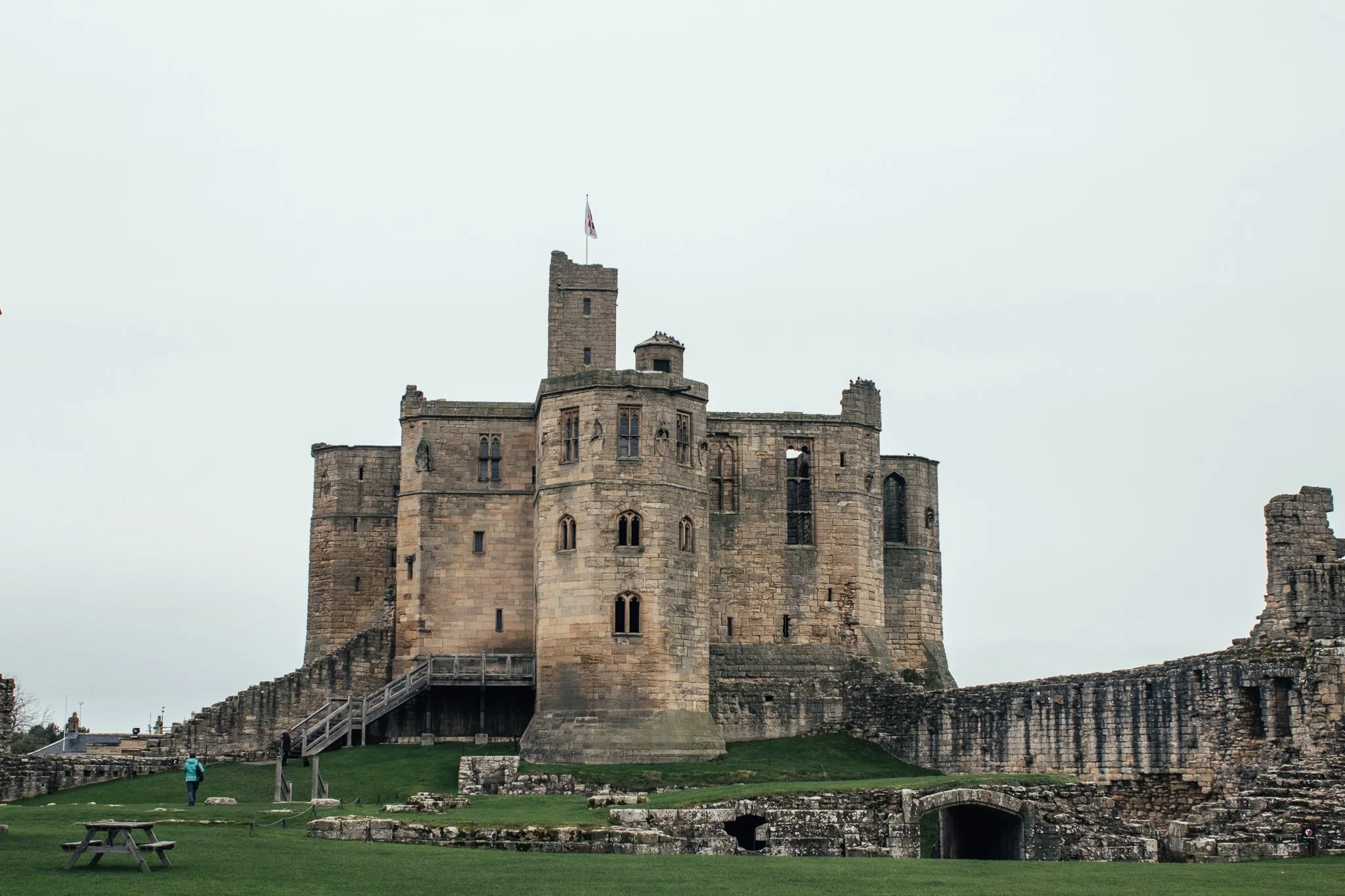 Ancient stone castle with battlements and tower, set on a grassy landscape under a cloudy sky.