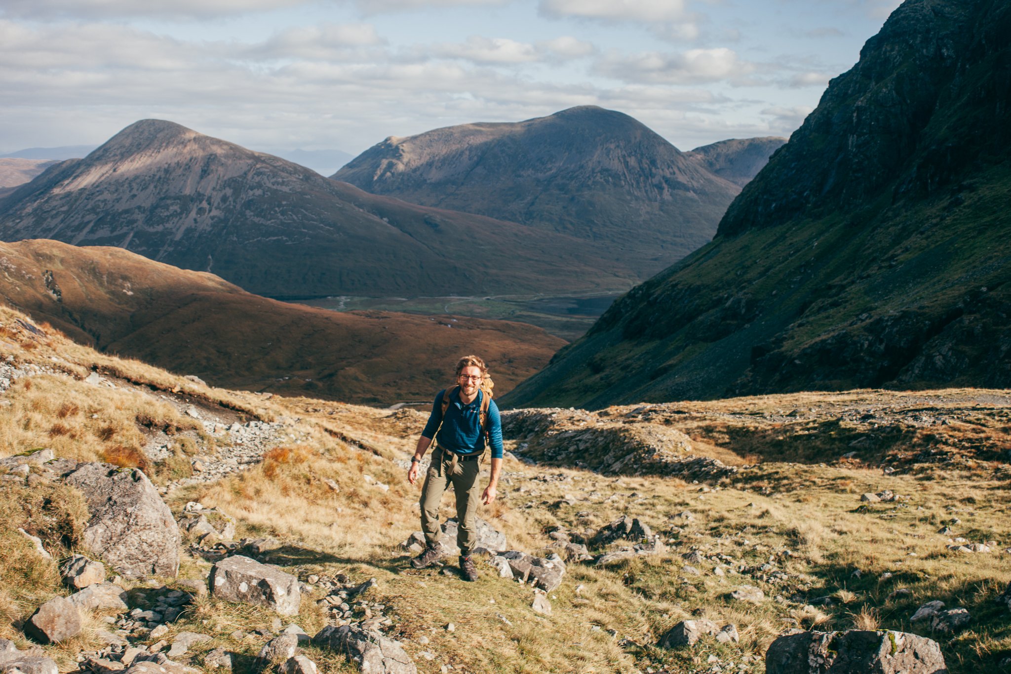 A person hiking in a mountainous landscape with rolling hills and large mountains in the background.