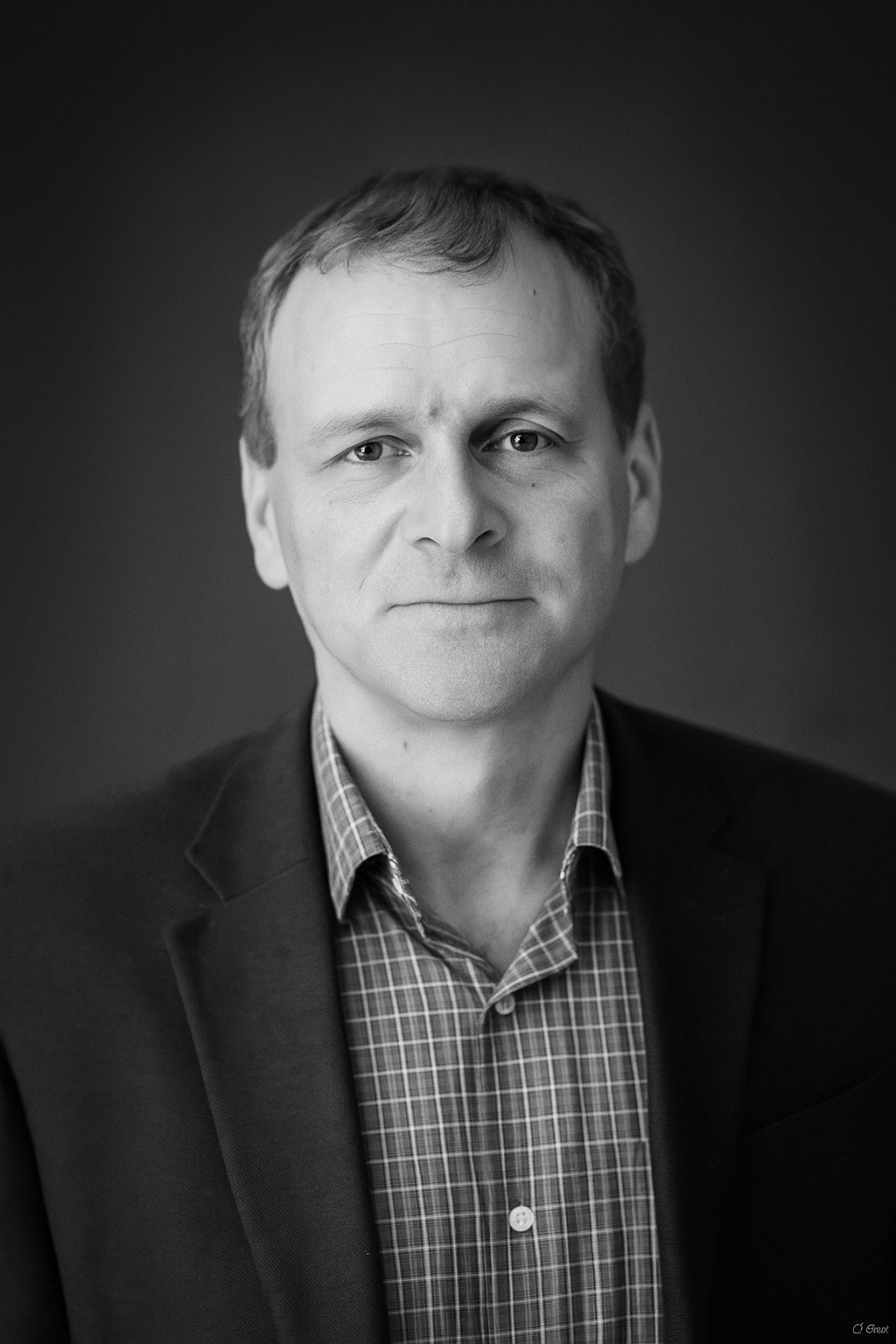 Black and white portrait of a middle-aged man in a suit and checkered shirt, looking at the camera with a slight smile.