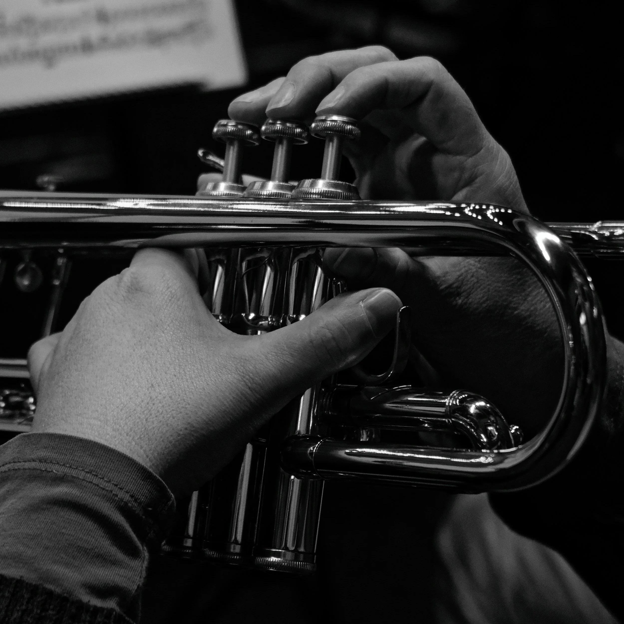 Black and white photo of a person playing a trumpet, focusing on their hands and the instrument.