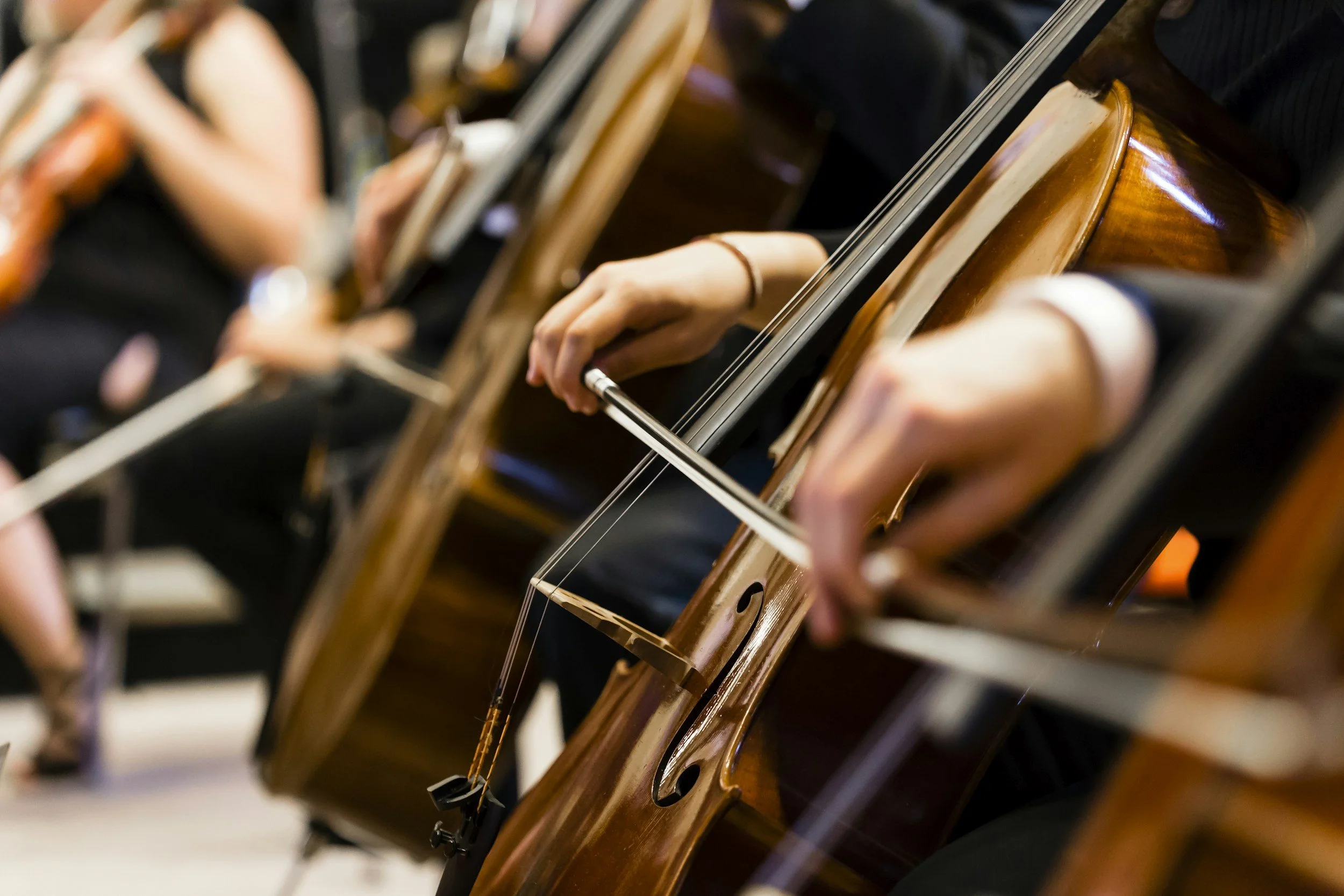 Close-up of a person playing a cello, focusing on their hand holding the bow and the cello's body.