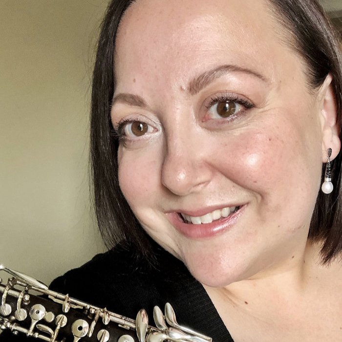 A woman with short dark hair and earrings, smiling, holding a silver flute.