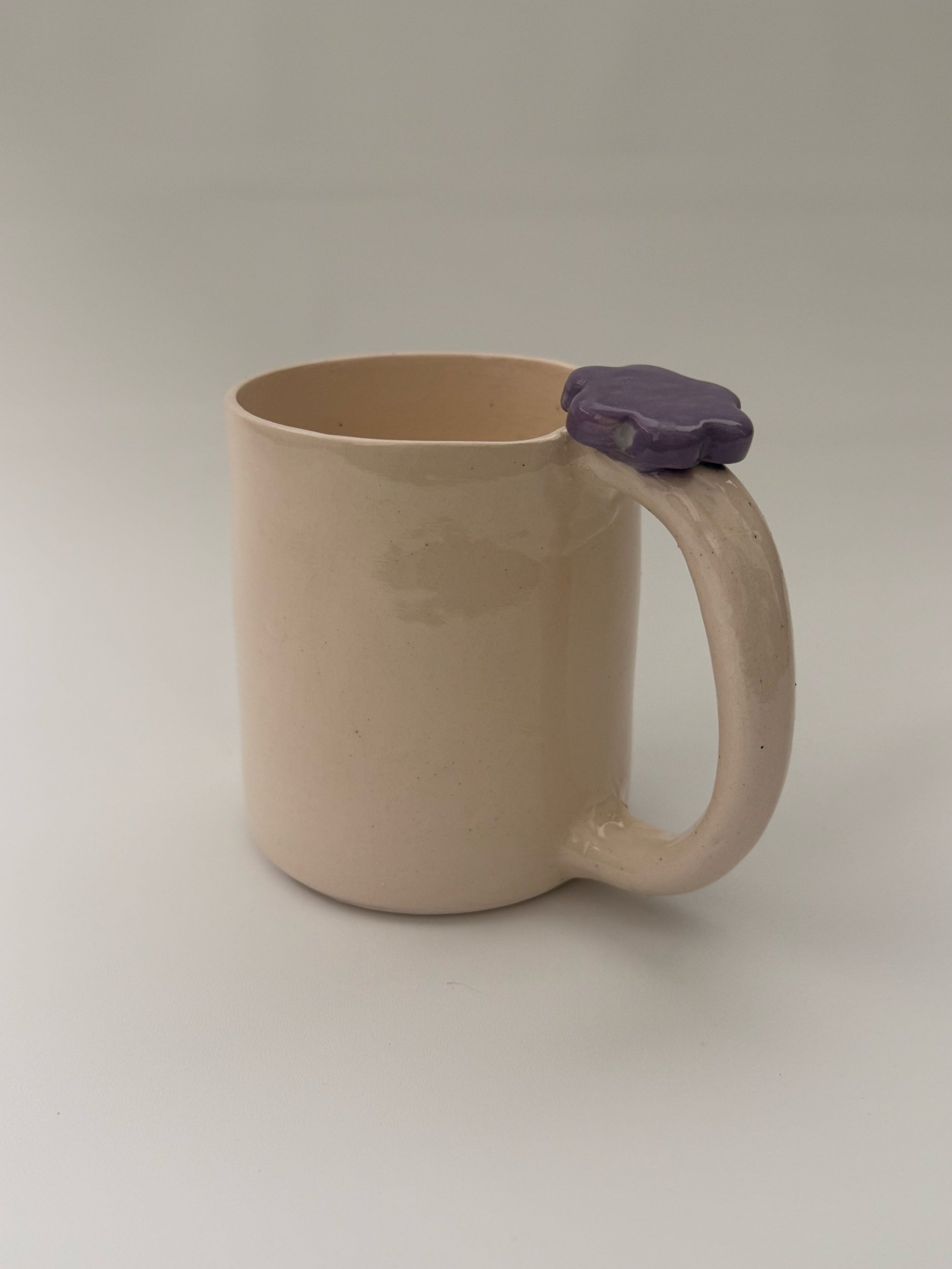 A ceramic porcelain mug with a purple flower on the top of the handle