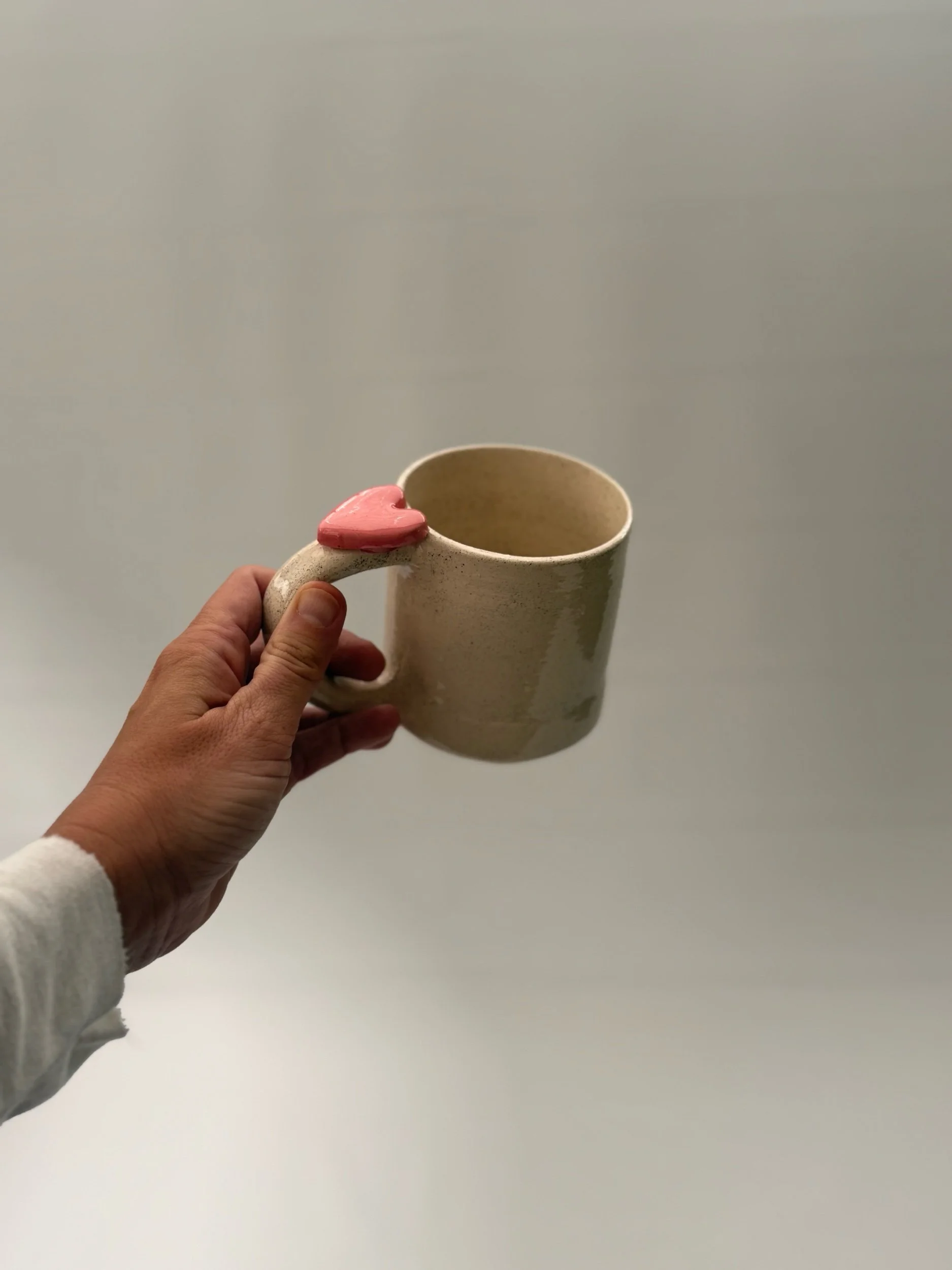 A kitchen countertop with seven handmade ceramic mugs, a gold faucet, a white farmhouse sink, beige cabinets with gold handles, a plant in a white pot, and a white subway tile backsplash.