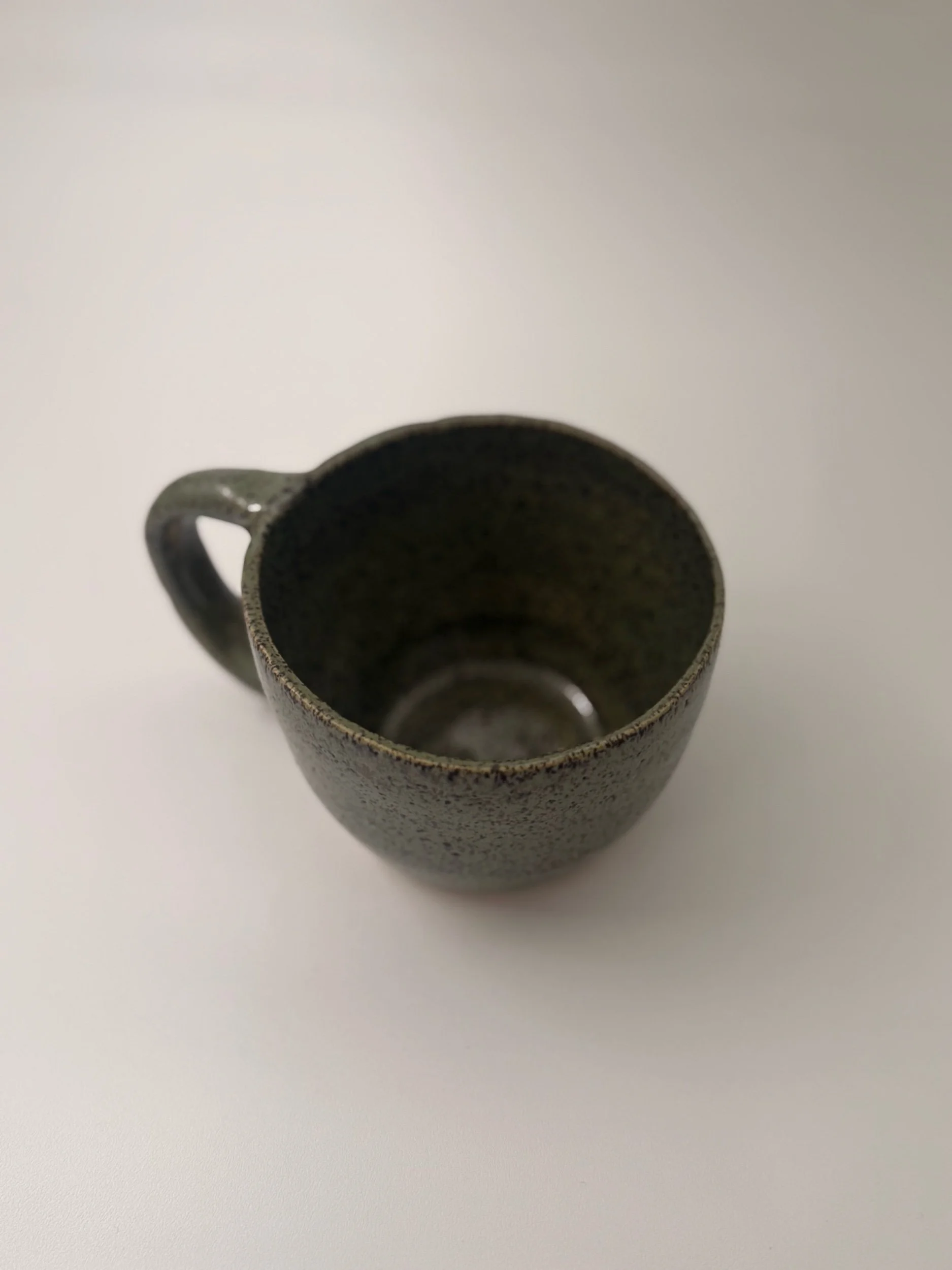 Ceramic object with a cylindrical shape, glazed top, and hole on the side, placed on a wooden surface against a light-colored wall.