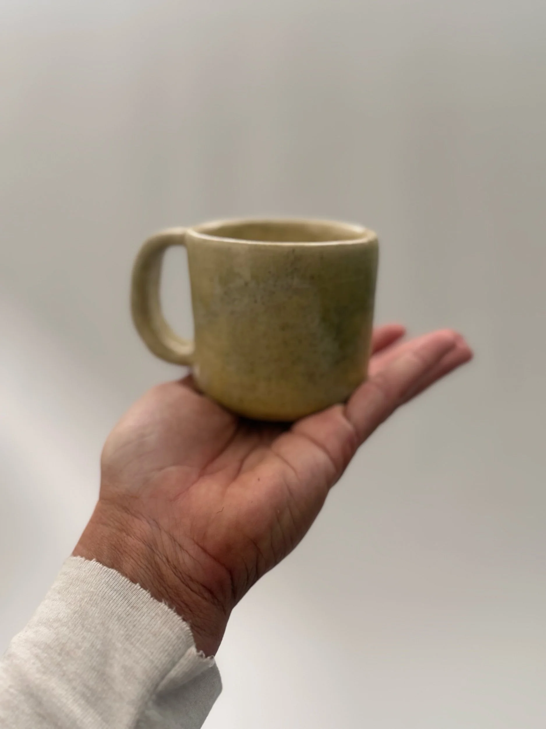 A white kitchen countertop with a gold faucet, beige cabinetry with gold handles, a small decorative ceramic vessel with blue and pink designs, and a small dish or bowl.