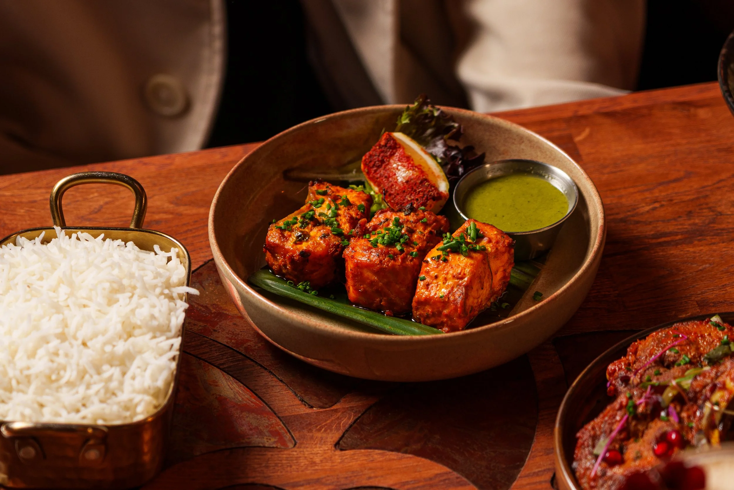 Plate of grilled salmon with green chutney, garnished with chopped herbs, served with a side of white rice and salad, on a wooden table.