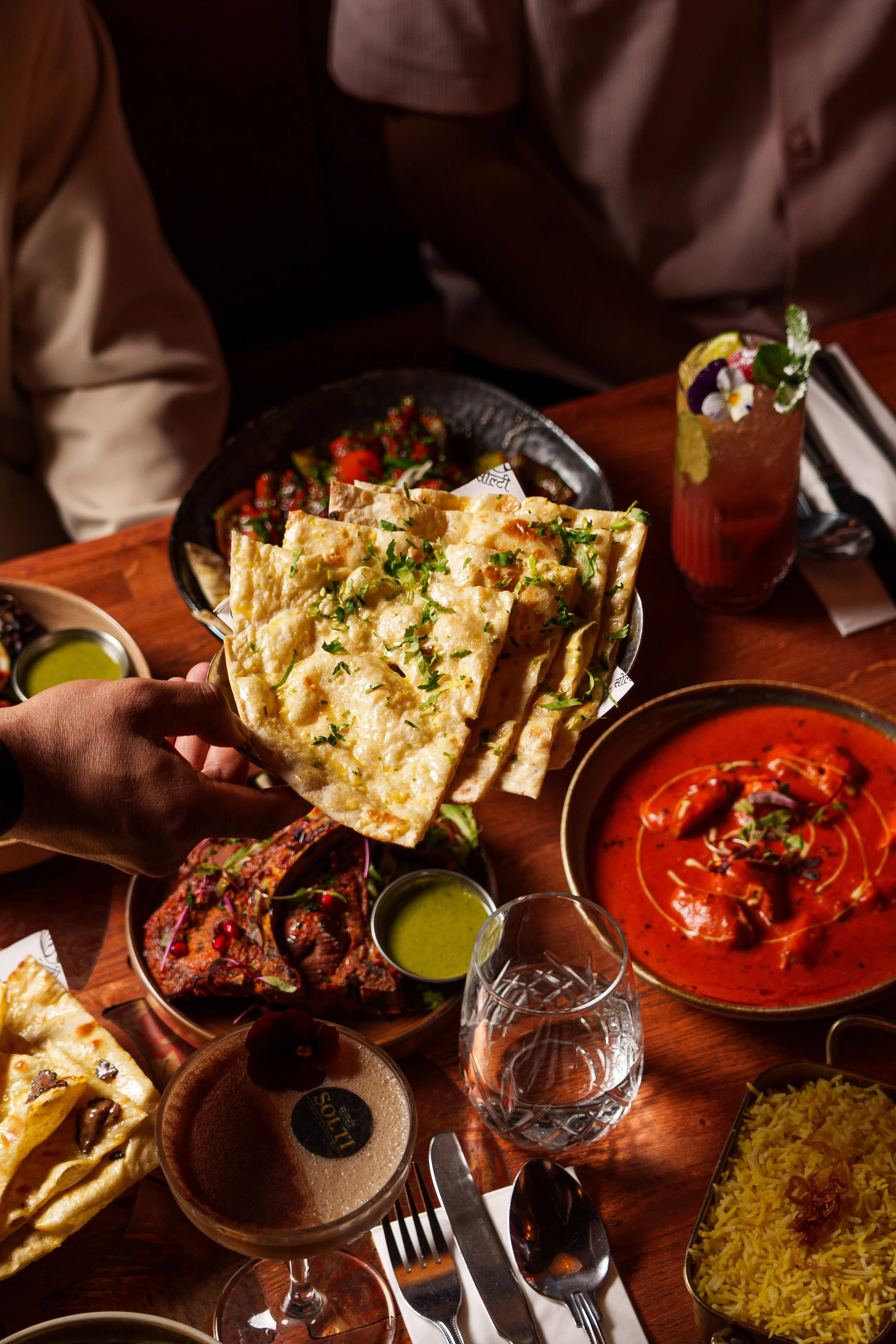 A table with various Indian dishes including naan bread, curry, rice, and drinks at a restaurant.