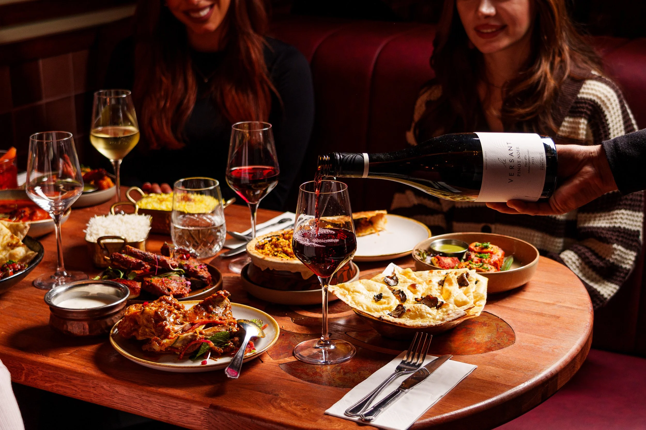 People enjoying a meal with various dishes and glasses of wine at a wooden table in a cozy restaurant
