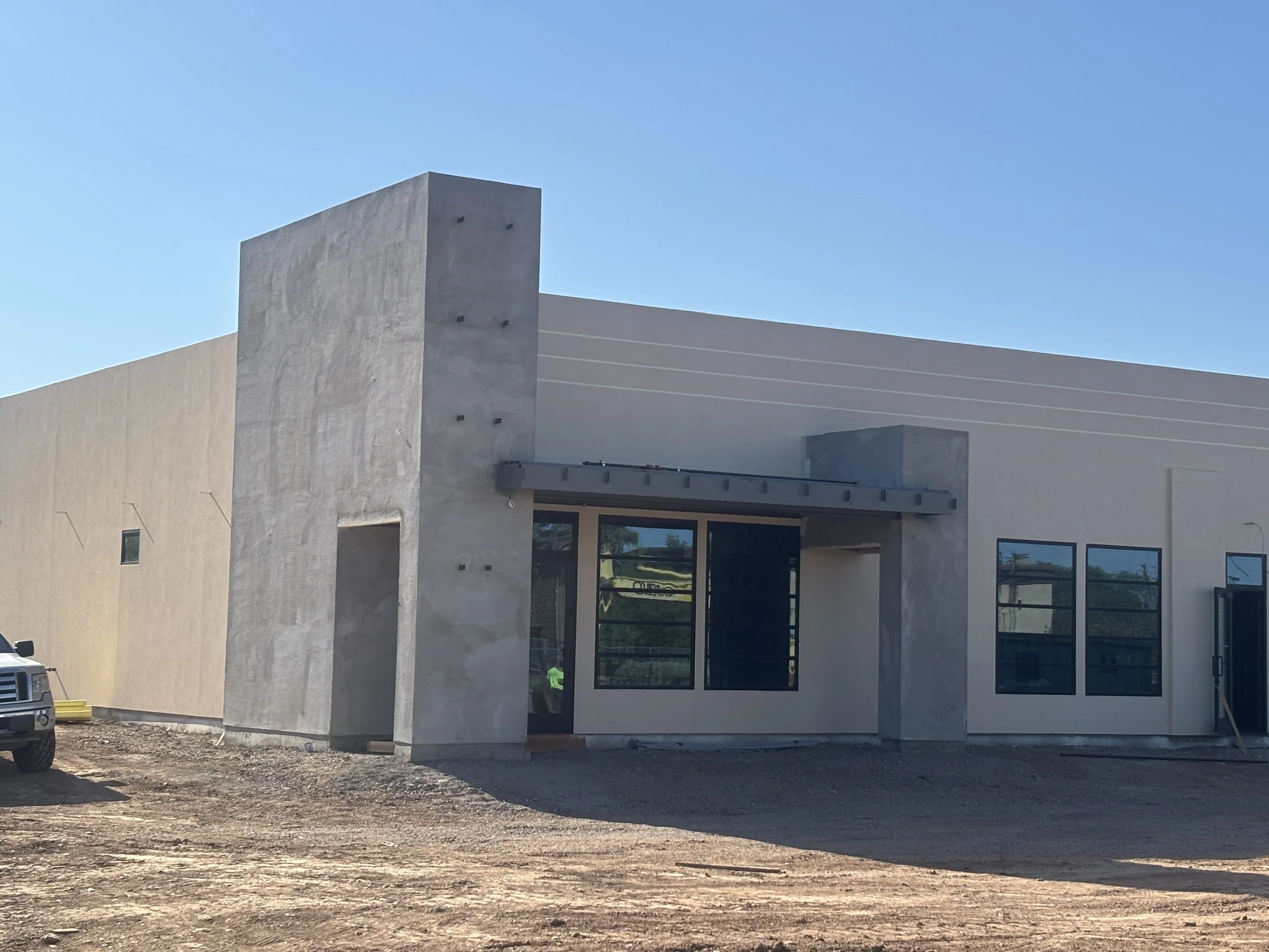 Exterior view of a modern building under construction with concrete walls, large windows, and a clear blue sky.