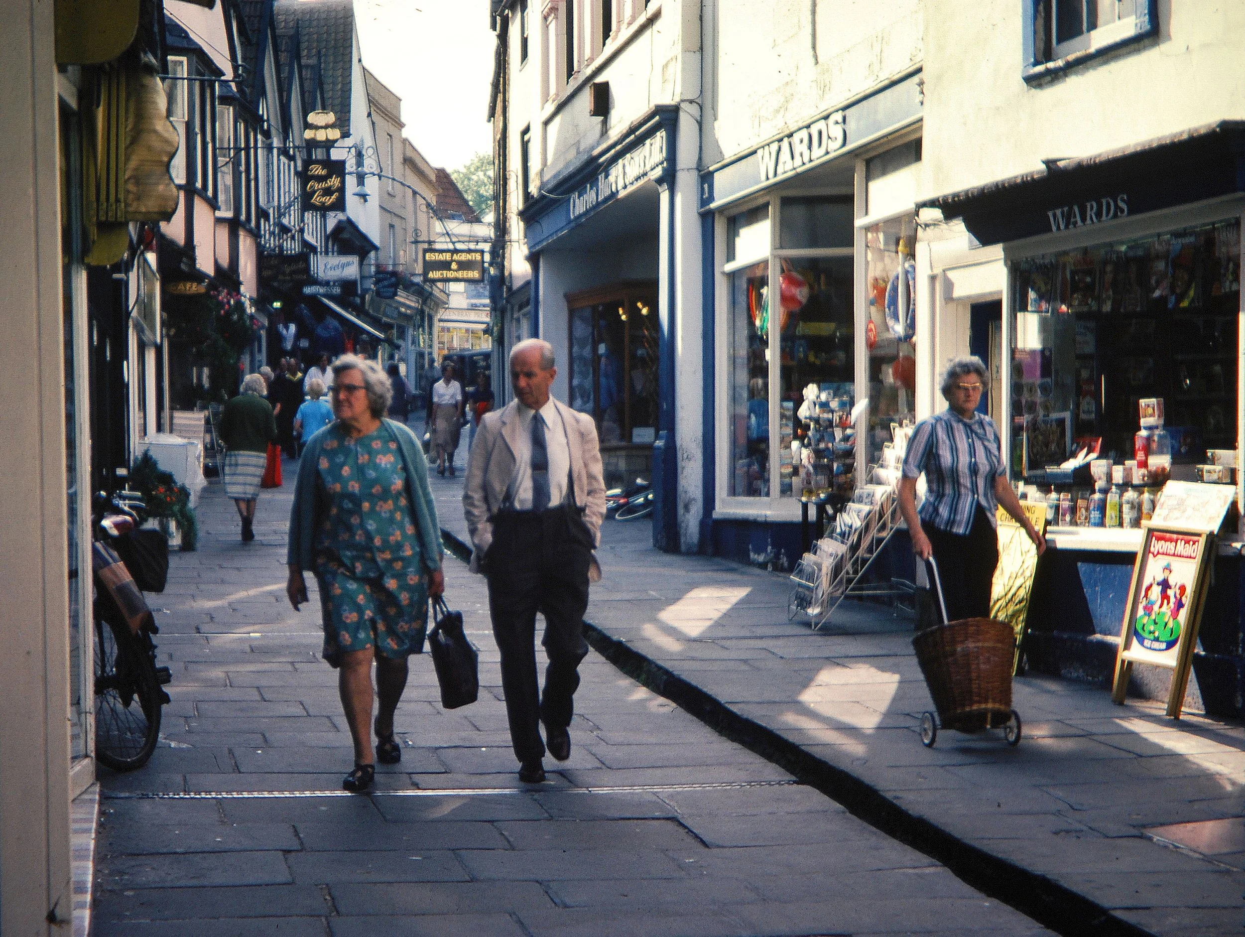  CHEAP STREET -  
This couple are strolling down unique Cheap Street with its gently flowing leat. There is Wards stationery and sweet shop, Charles Hart the jewellers, The Crusty Loaf bakery and Evelyns clothing store.
