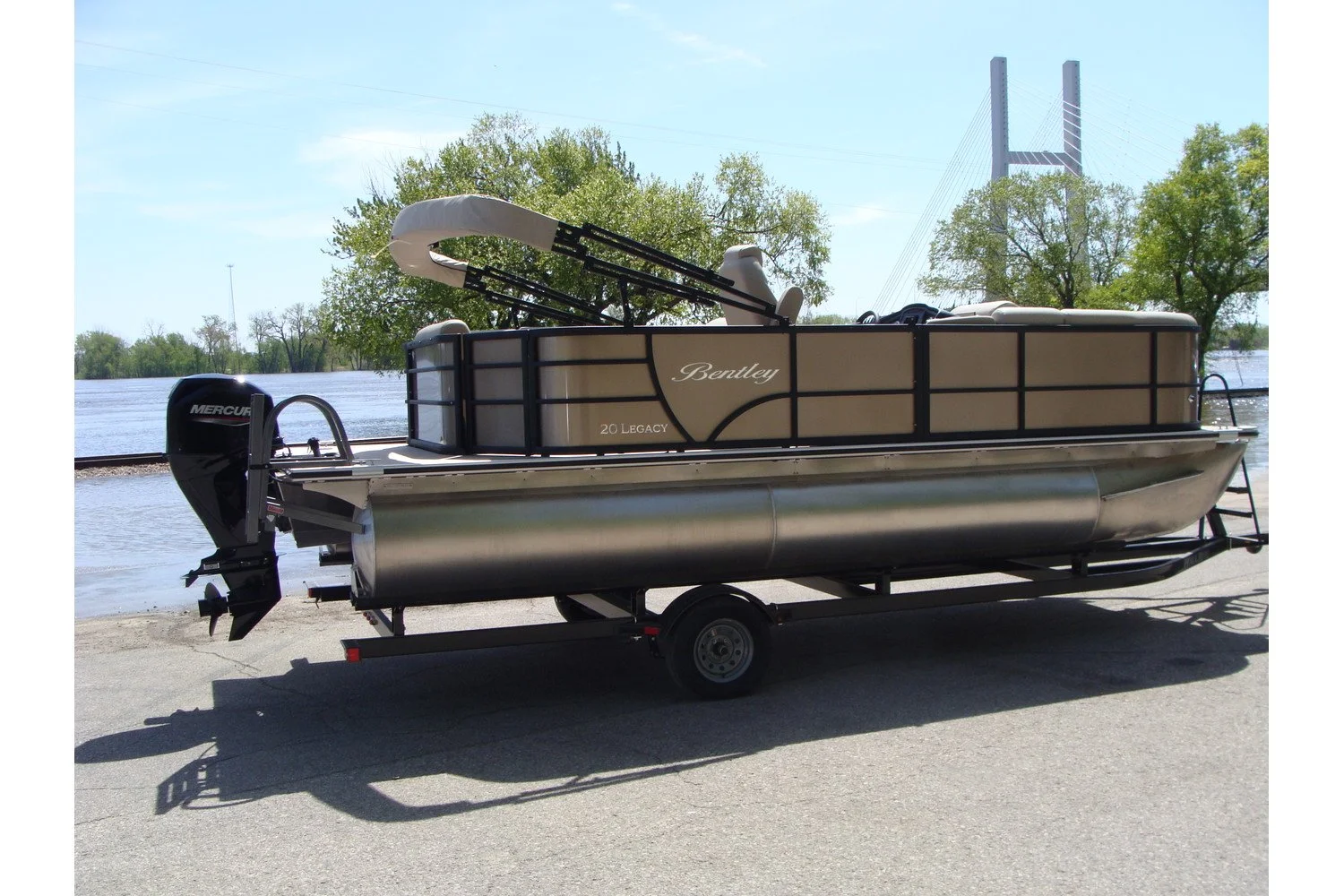 A pontoon boat on a trailer with a river and bridge in the background
