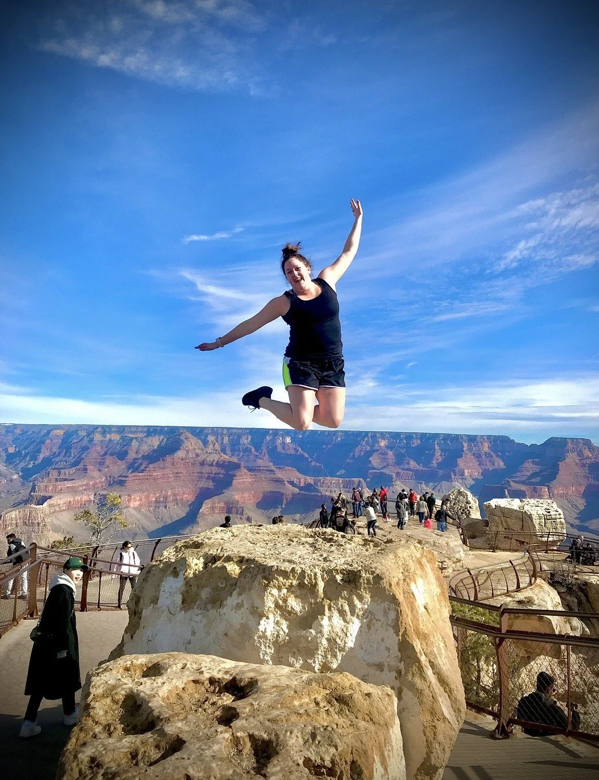 A woman jumping in the air at a scenic overlook with a canyon-like landscape in the background.