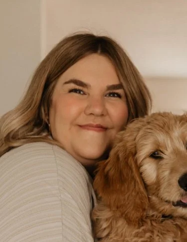 A woman smiling and cuddling with a golden retriever puppy.