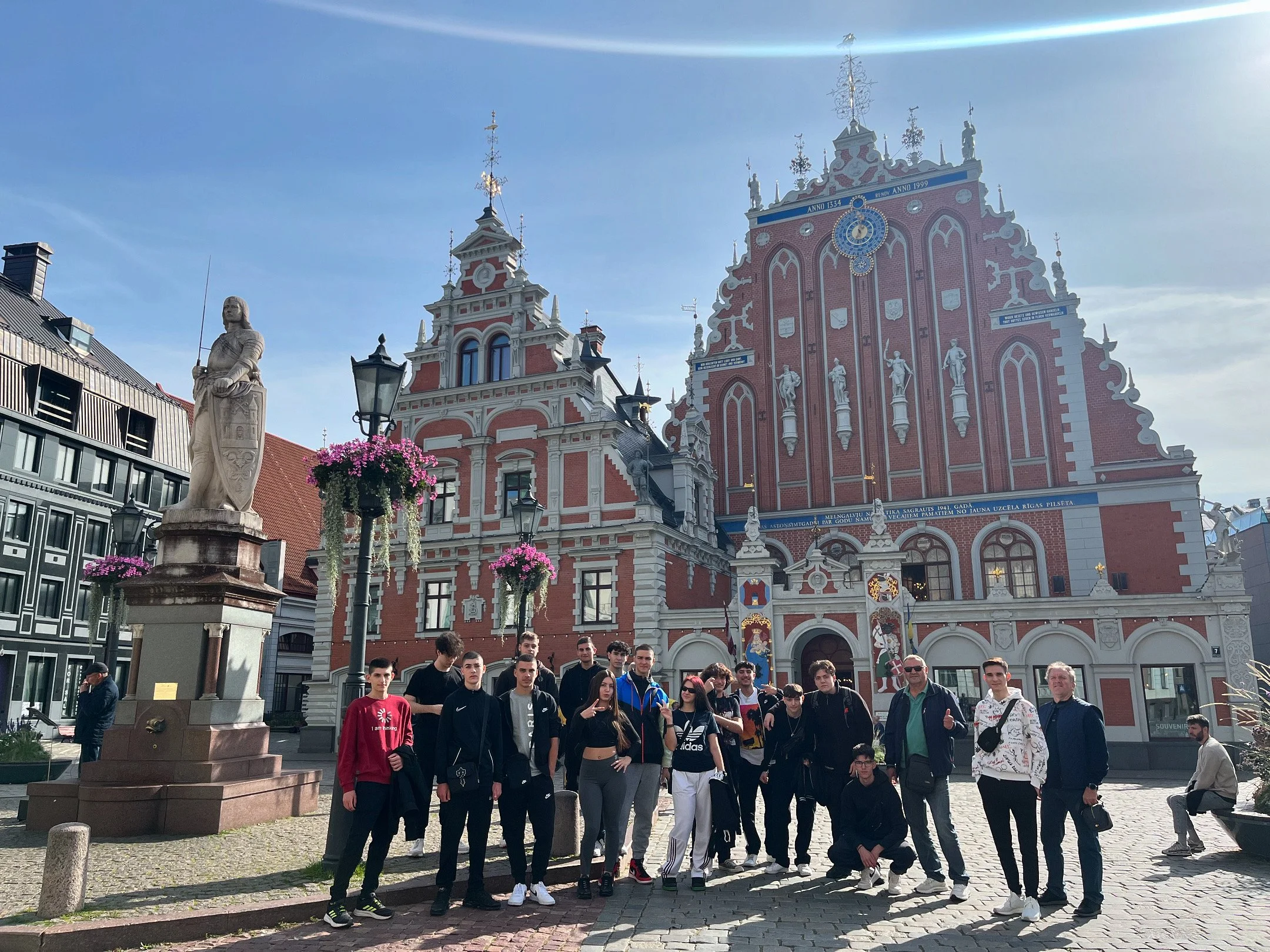 A group of young people posing in front of historic buildings with intricate architecture and statues on a sunny day.