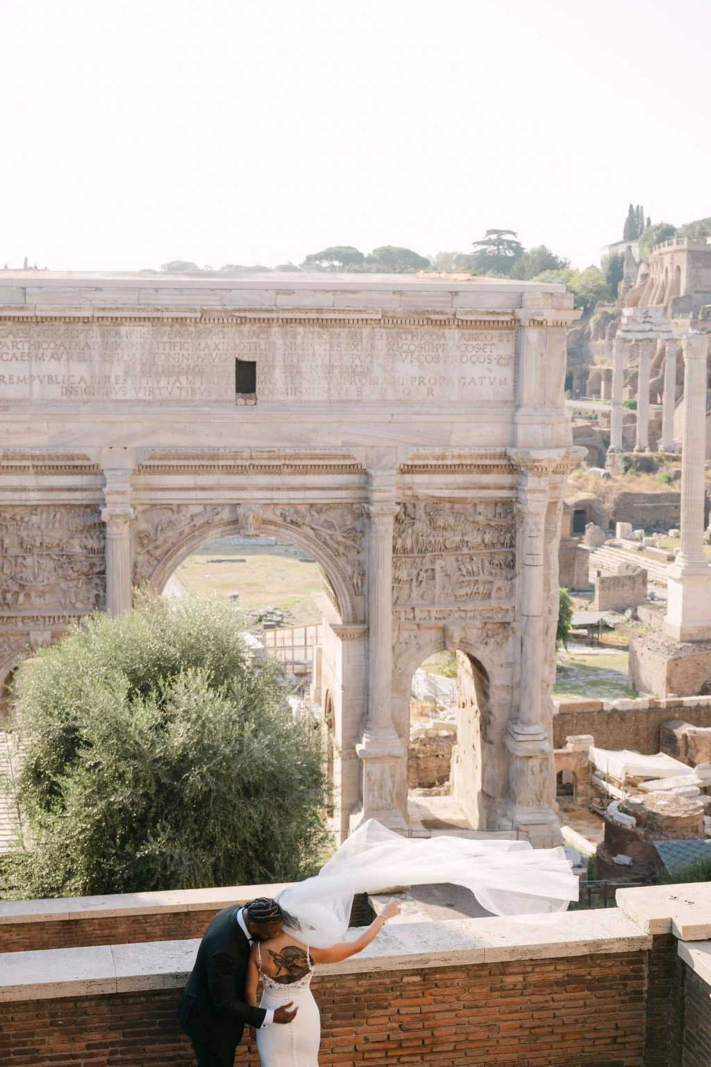 sarapaolucci-groom-kissing-bride-shoulder-veil-flying-in.the-wind-in-front-of-foro-romano.jpg
