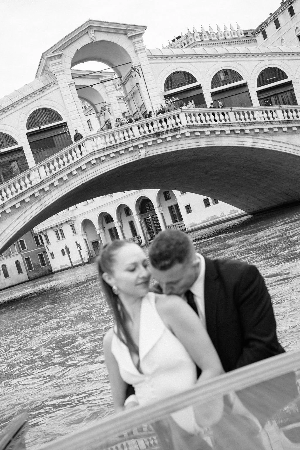 sarapaolucci-groom-kissing-bride-shoulder-in-front-of-rialto-bridge-in-venice.jpg