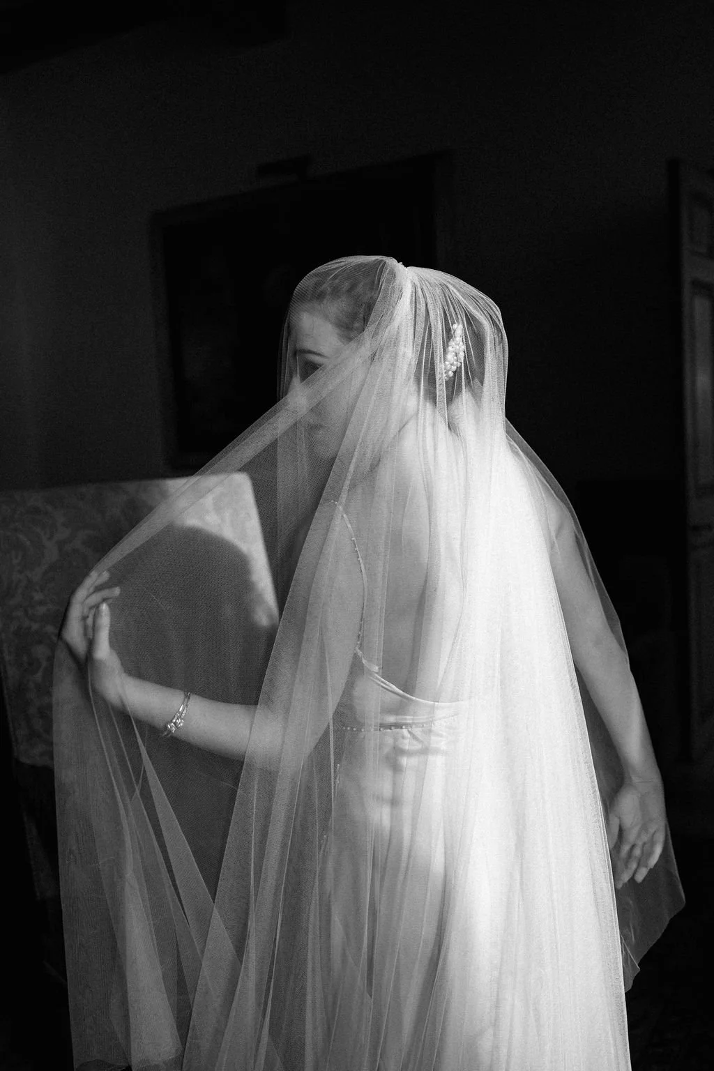 A bride in a wedding dress and veil adjusting her veil inside a room.
