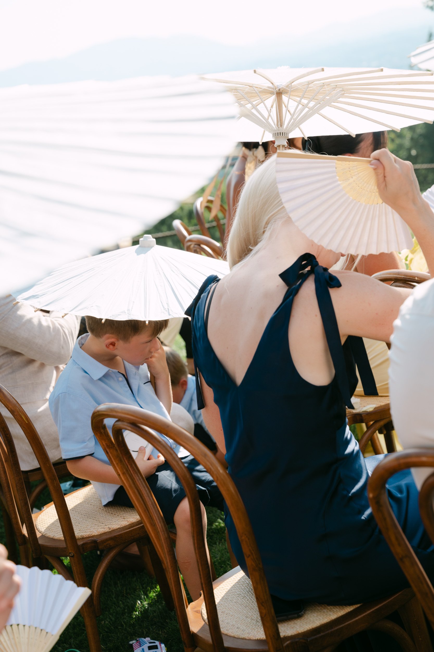People sitting outdoors under white umbrellas, some with traditional Japanese paper umbrellas, enjoying a sunny day.