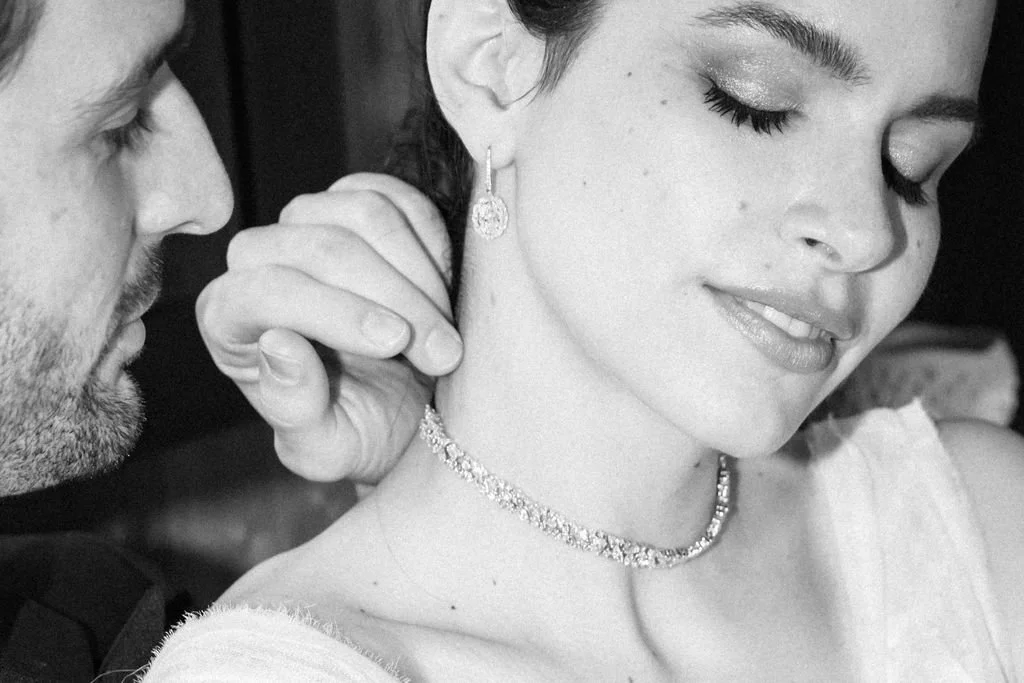 A woman with her eyes closed, smiling softly, as a man adjusts her earring.