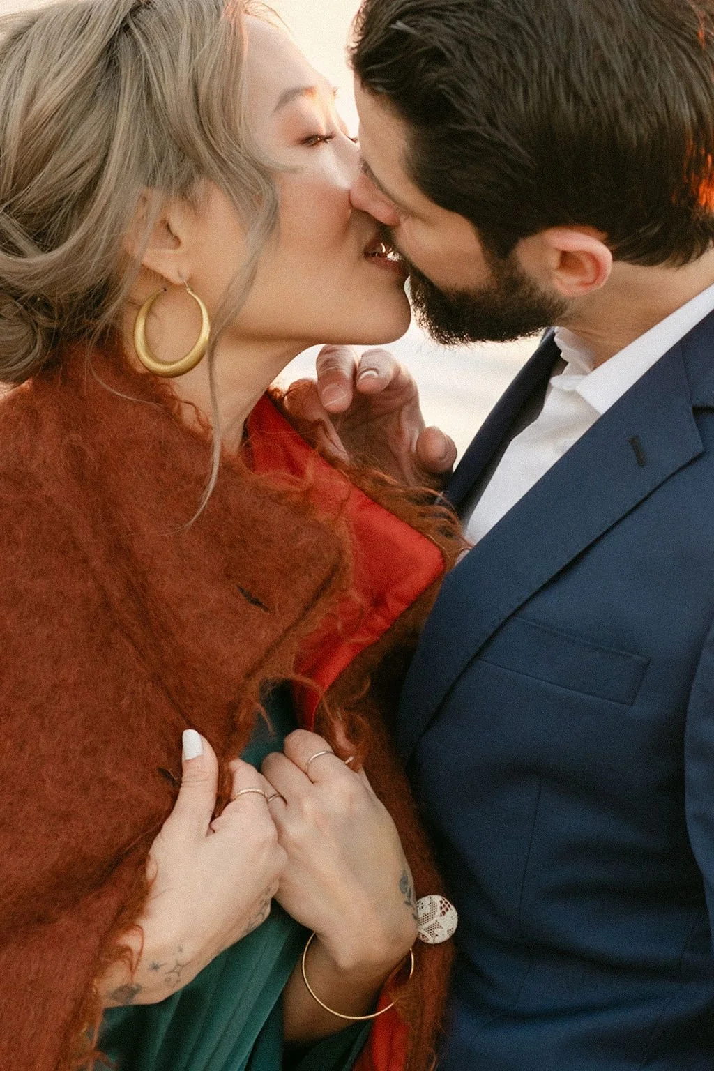A woman and a man are sharing a close, intimate kiss outdoors during sunset.
