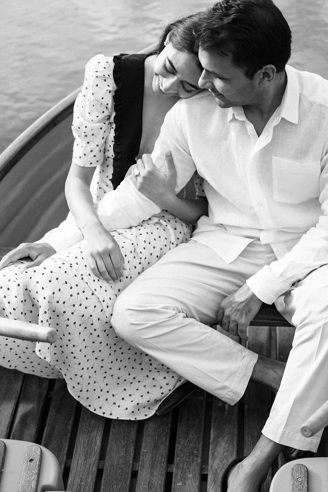 A black and white photo of a couple sitting together on a boat deck, smiling and leaning close to each other.