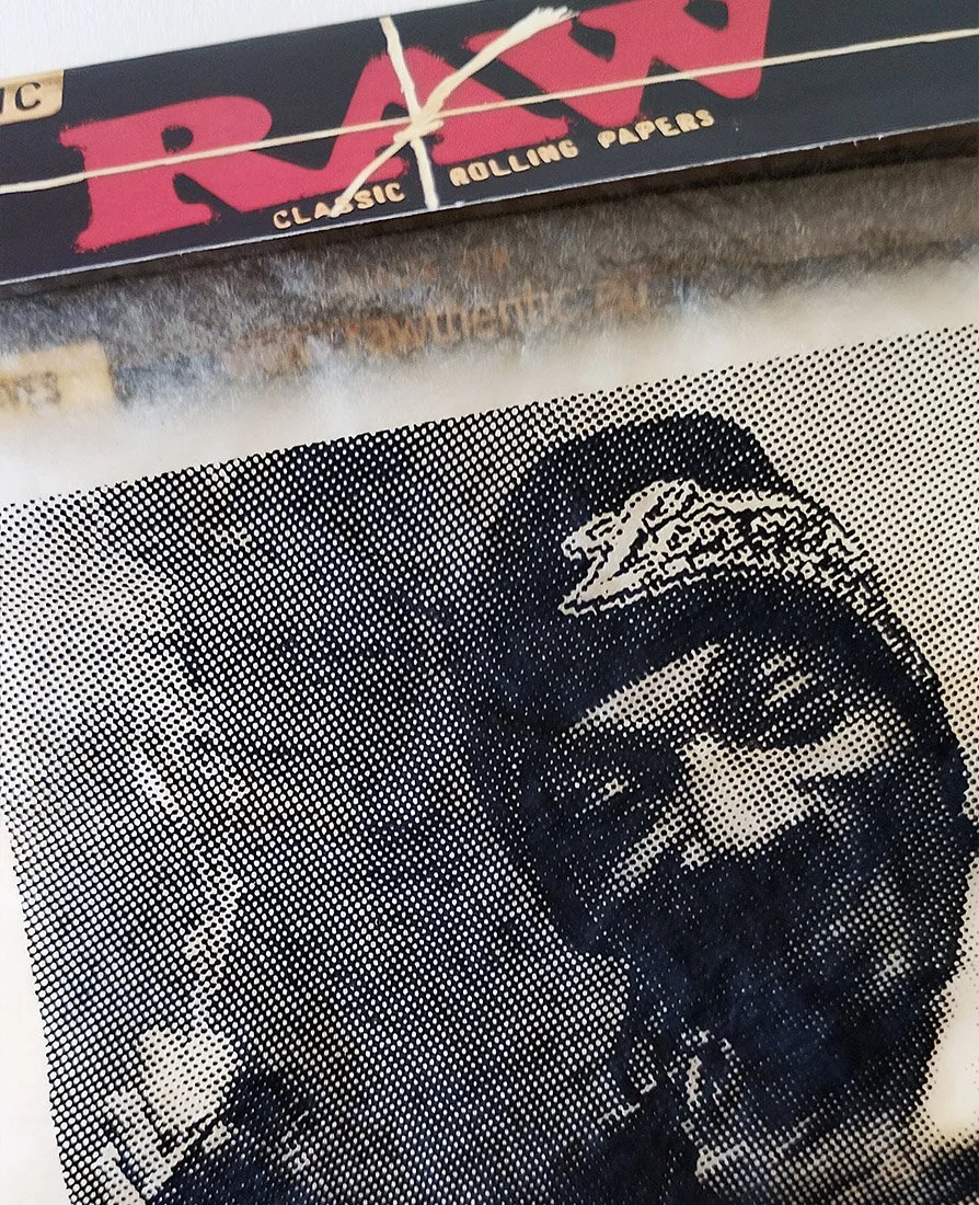 Close-up of artwork by Richard Pendry in a black box frame. A black-and-white halftone portrait of Snoop dog smoking a cigarette is screenprinted onto a sheet of Rizla-style rolling papers