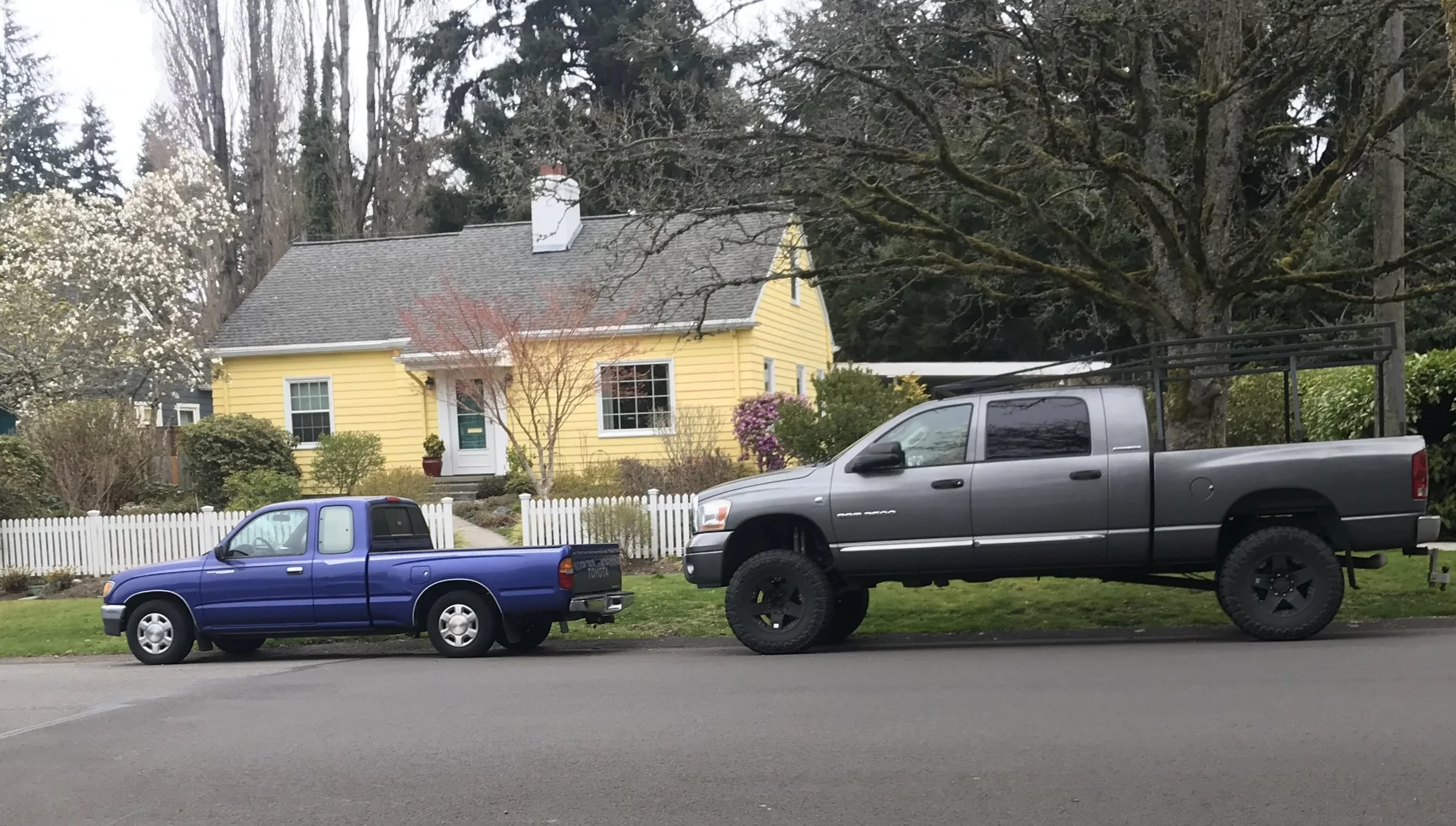 picture of a very small truck and a very large truck parked next to each other with a yellow house in the background