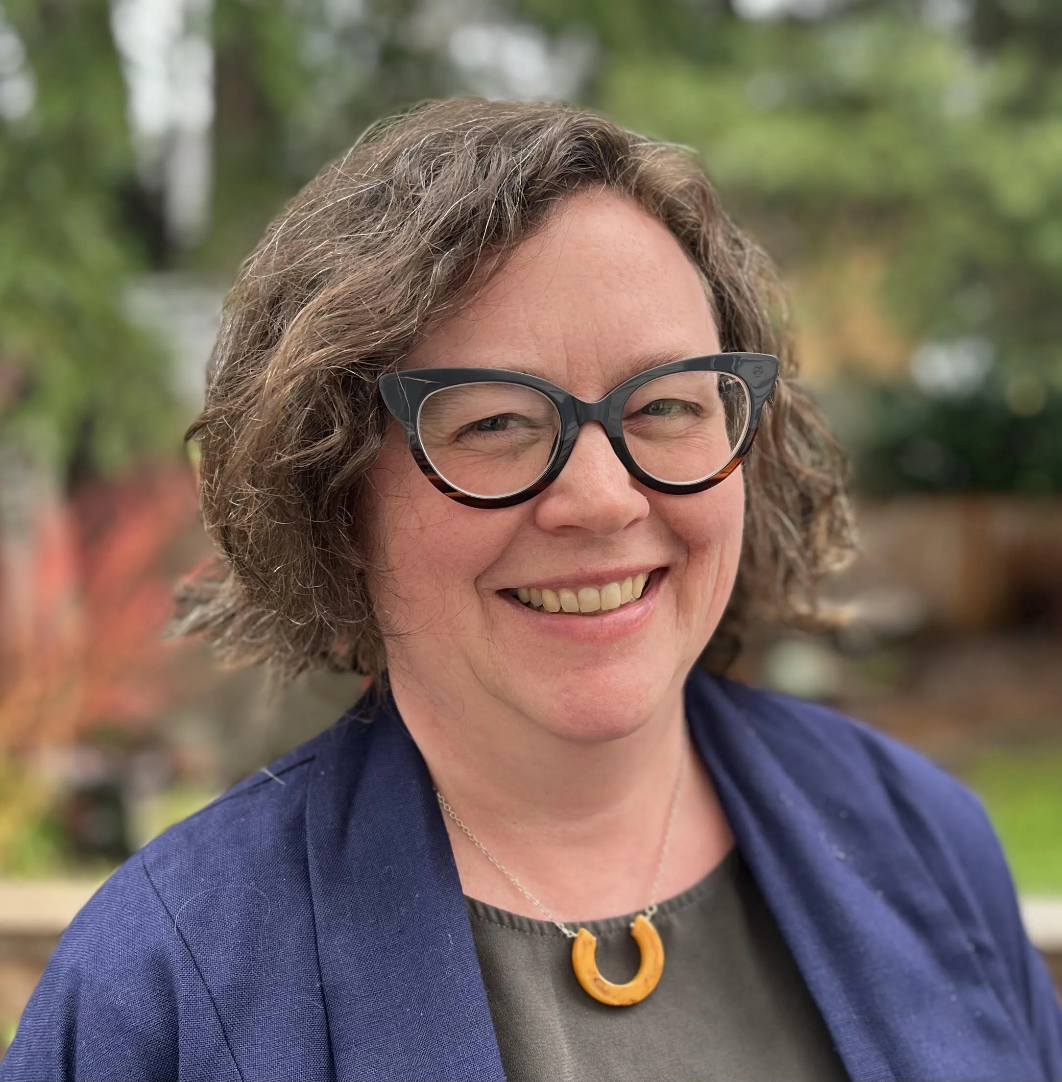 Photo of Catie Bull in a blue jacket with a yellow horseshoe necklace and a big smile