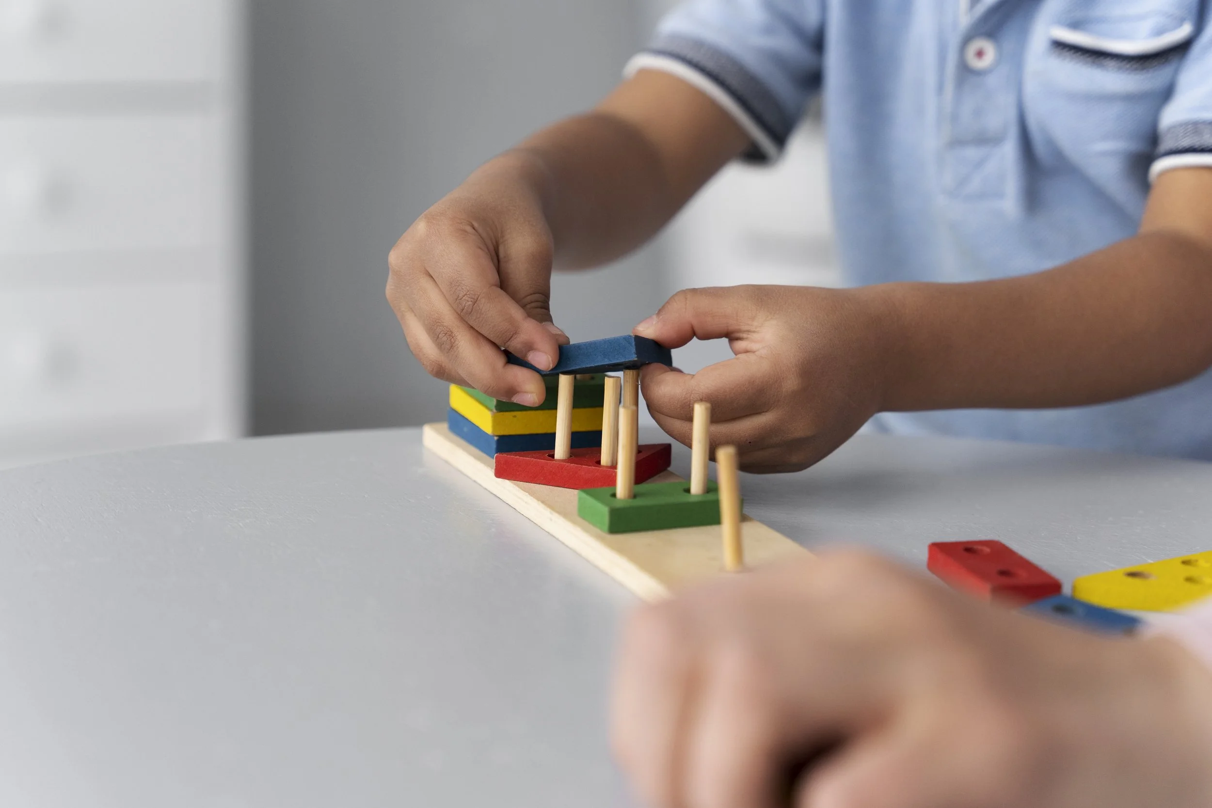 Child playing with colorful wooden stacking game on a white table.