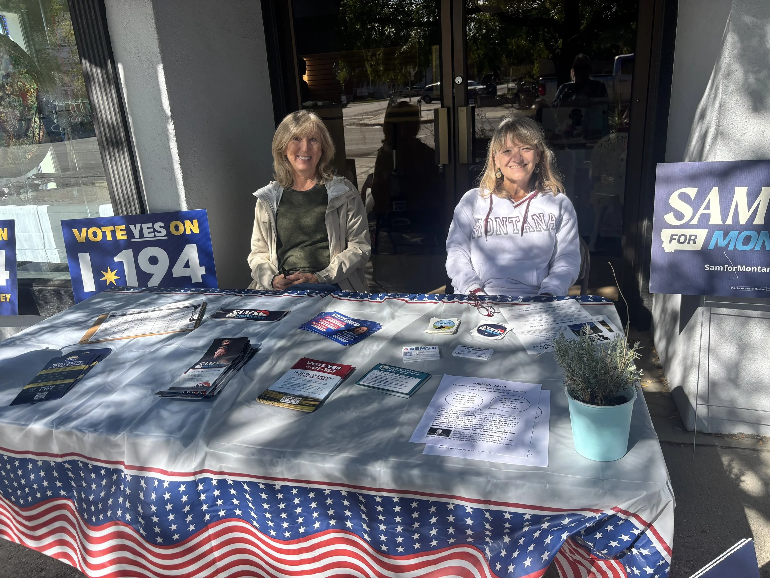 People participating in a voting event outside Adams Center, with tables, pamphlets, and sign-up sheets.