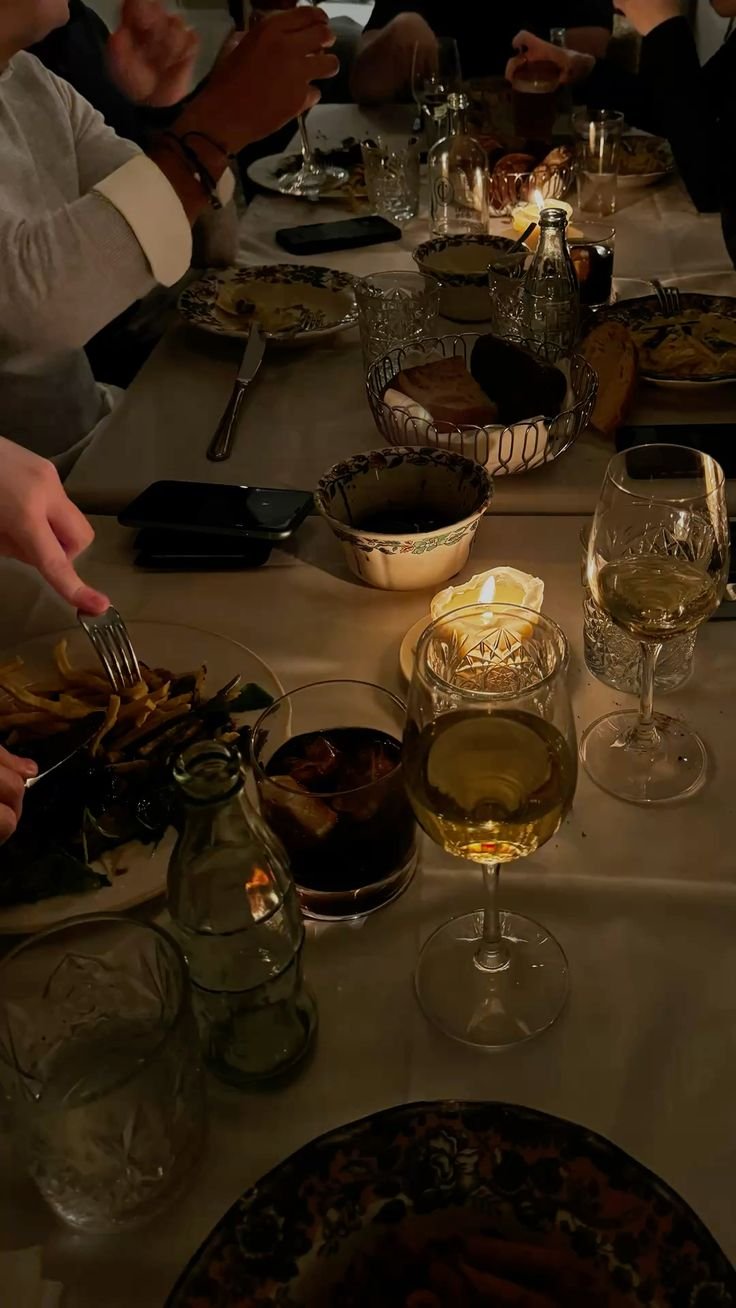 A dinner table set with wine glasses, plates, bowls, and candles, with people enjoying a meal.