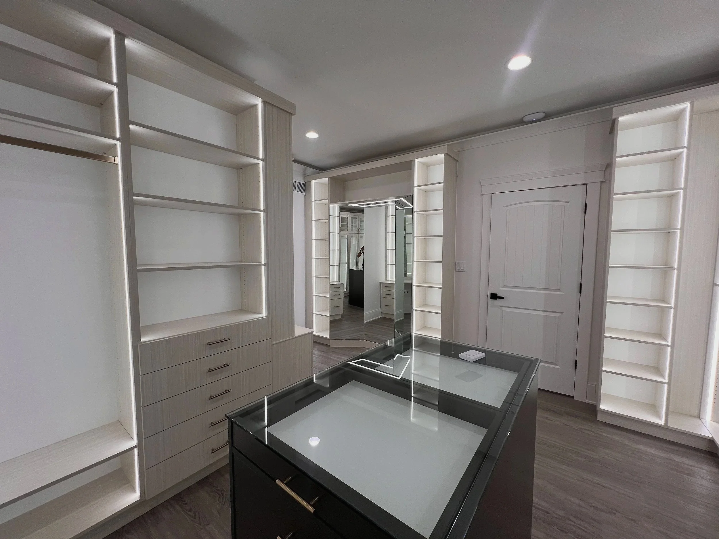 White custom walk-in closet with dark glass-top center island and built-in shelving