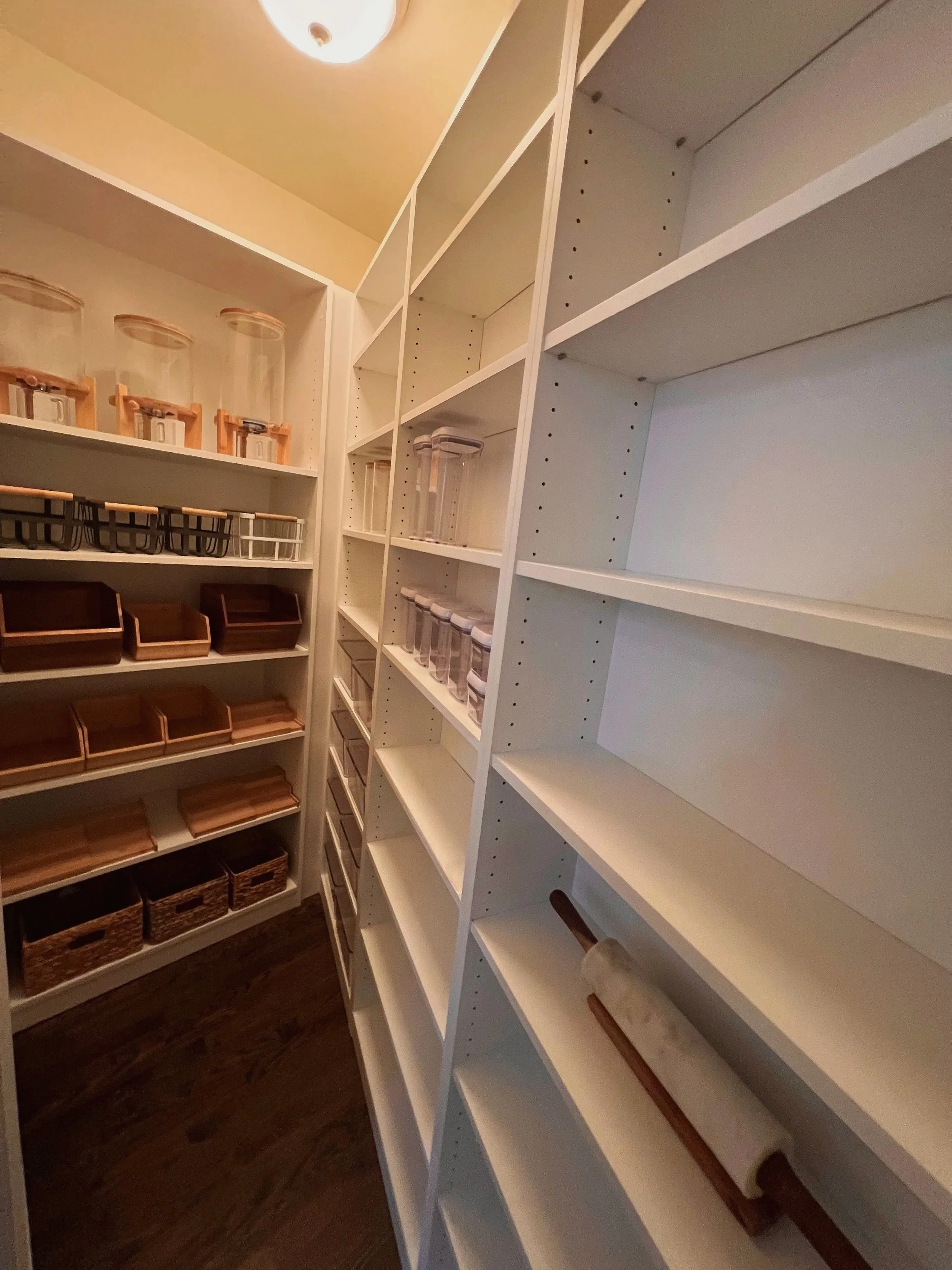 Narrow walk-in pantry with deep white shelves and wood floor