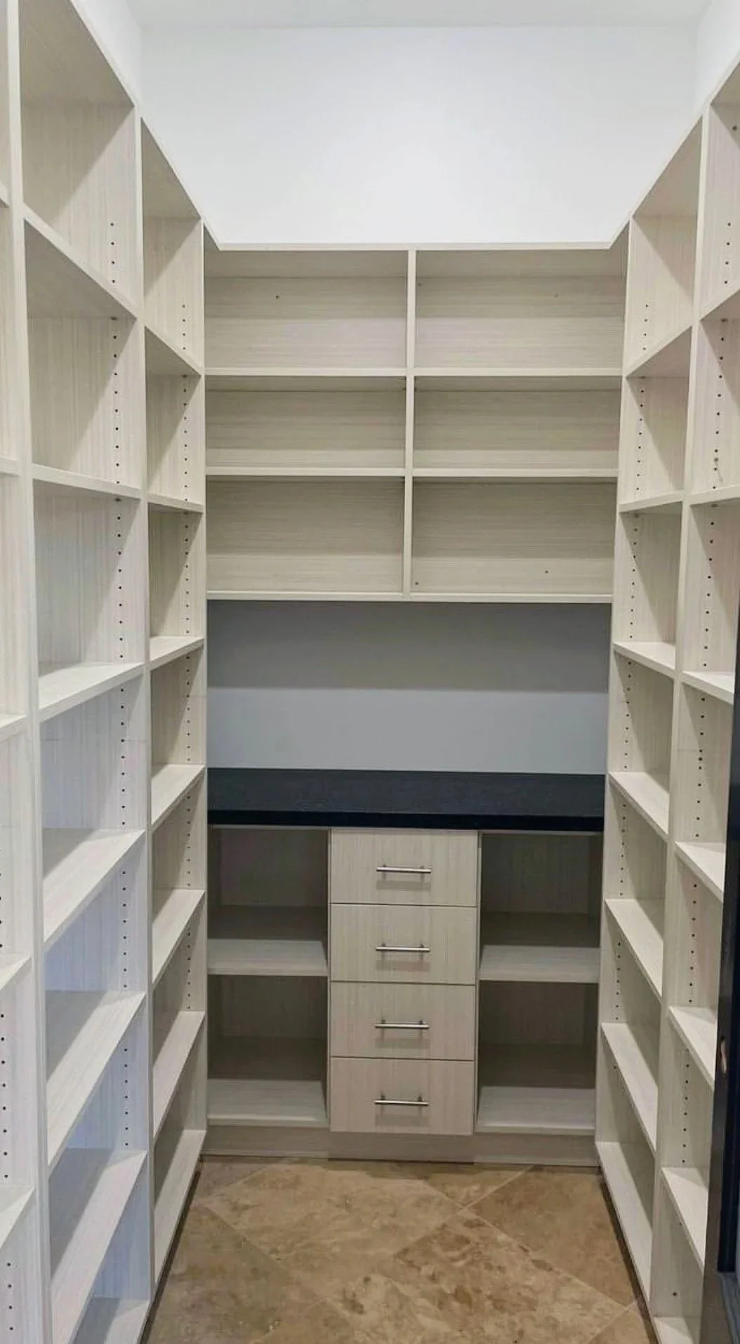 Tall light-wood pantry shelving with center drawers and dark countertop
