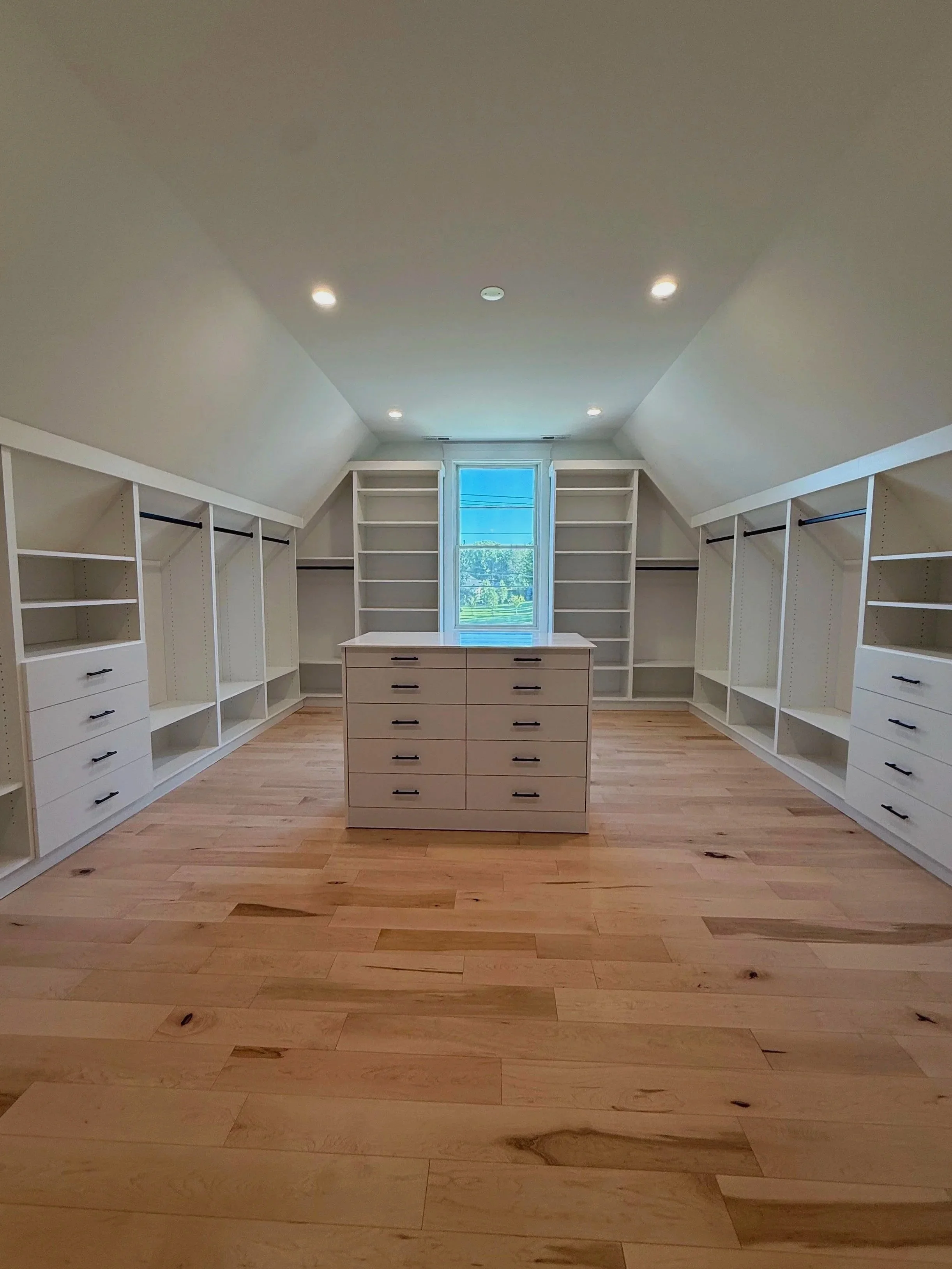Spacious white custom walk-in closet with center island and window in vaulted ceiling room