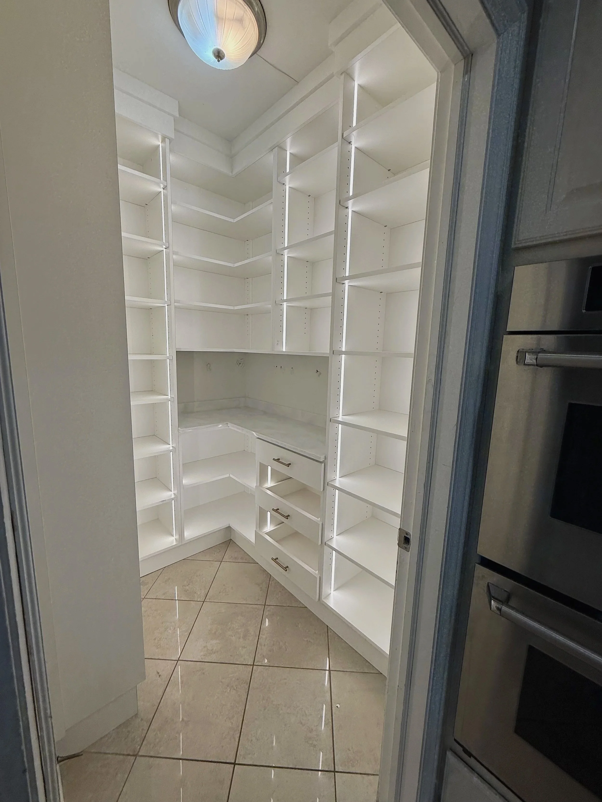Corner walk-in pantry with wraparound white shelving and tile floor