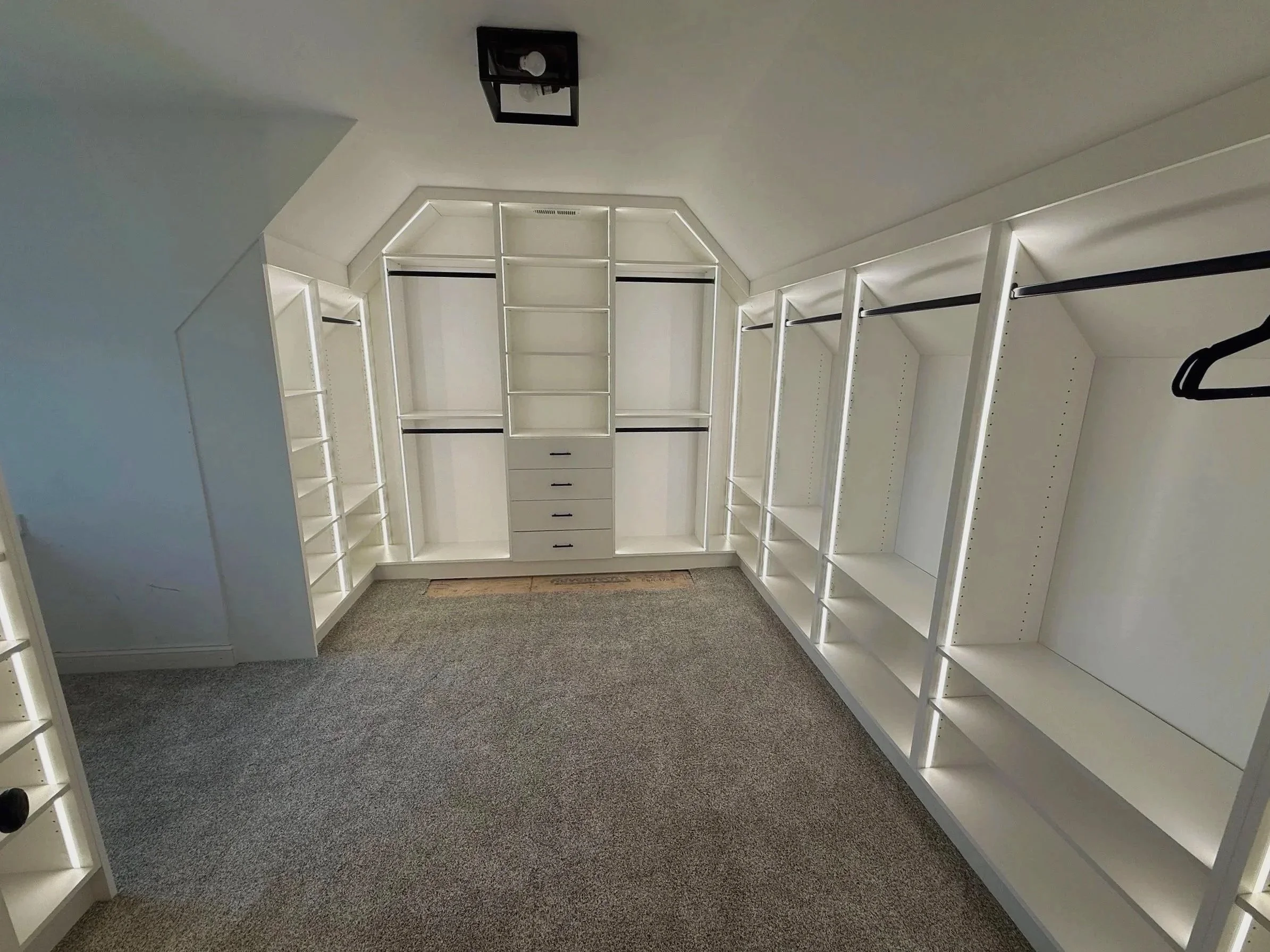 Carpeted white custom walk-in closet with sloped ceiling and wall-to-wall hanging rods
