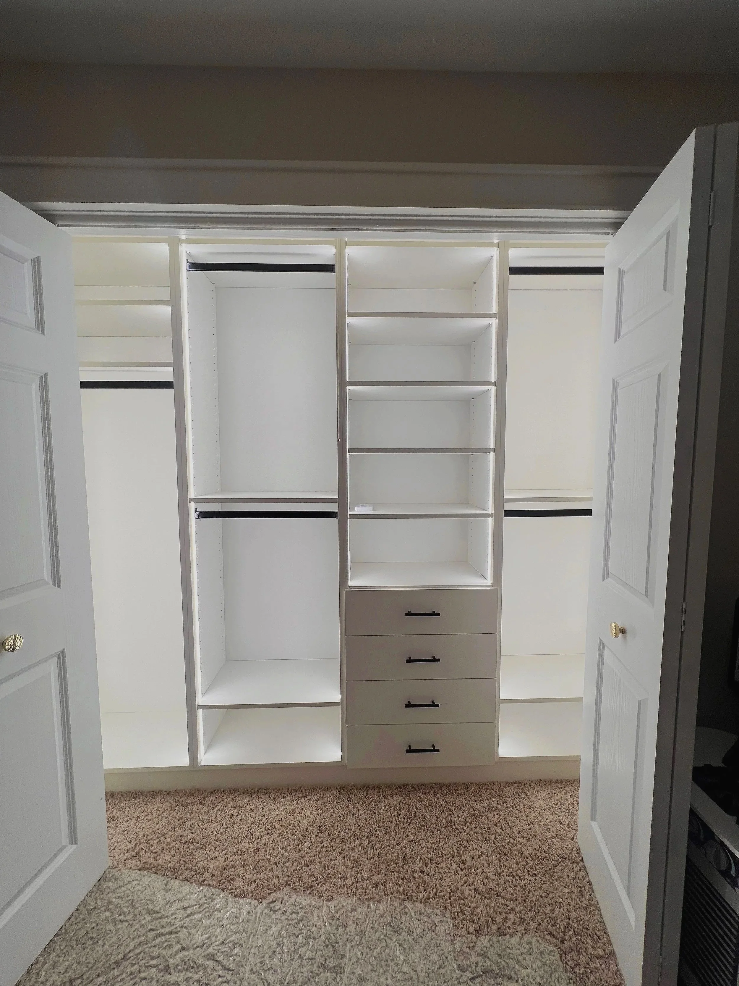 LED-lit white reach-in custom closet with hanging space and drawers on carpet