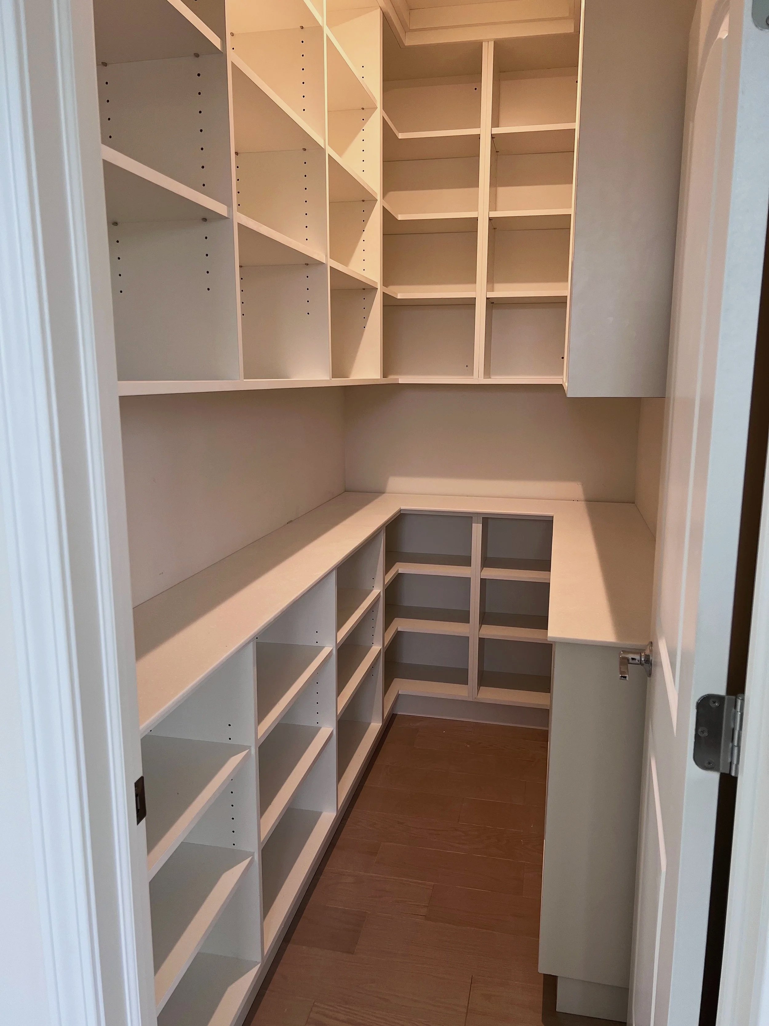 Long L-shaped walk-in pantry with white shelves and base cabinets
