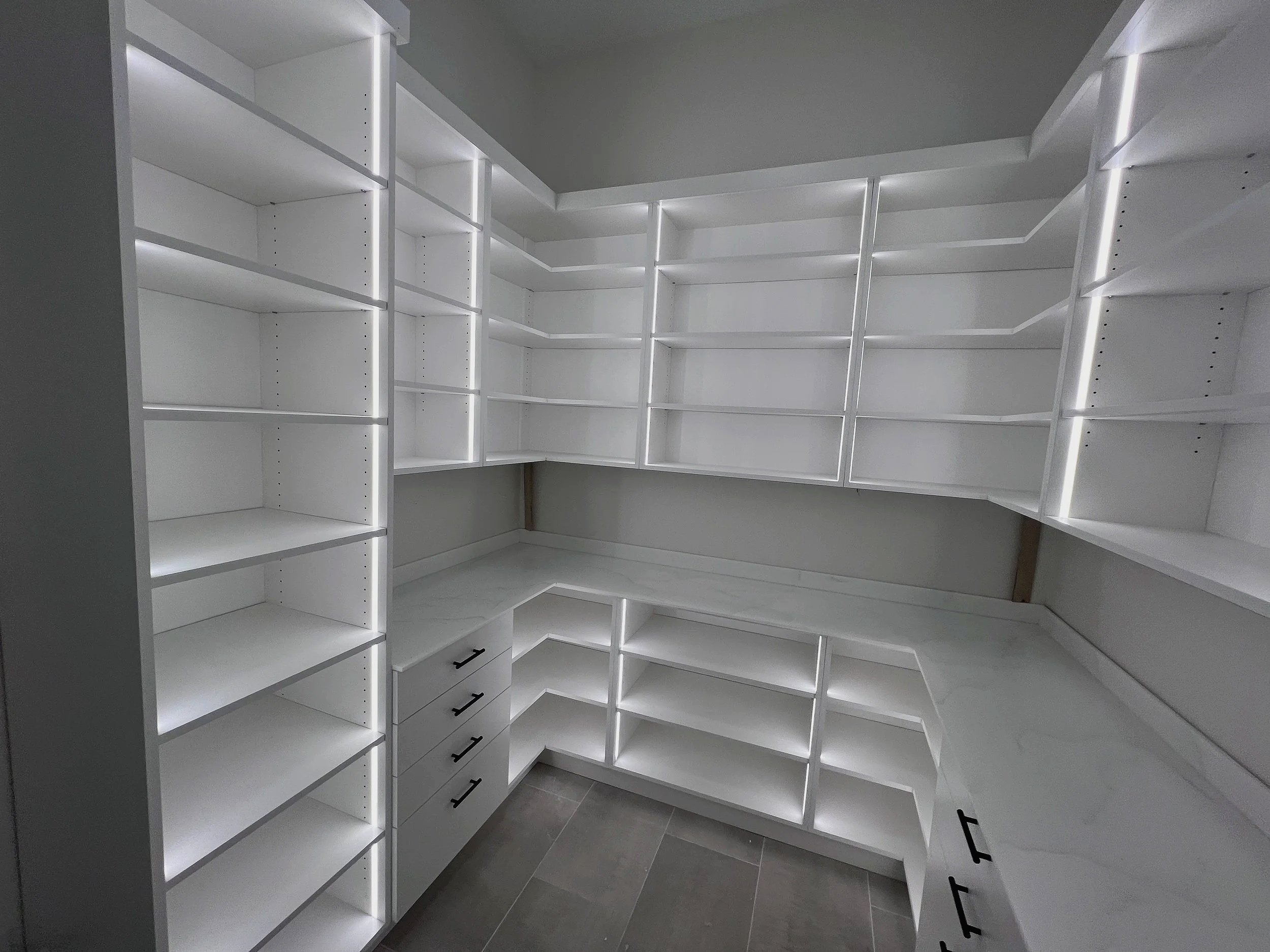 L-shaped custom pantry with white shelves, drawers, and LED accent lighting