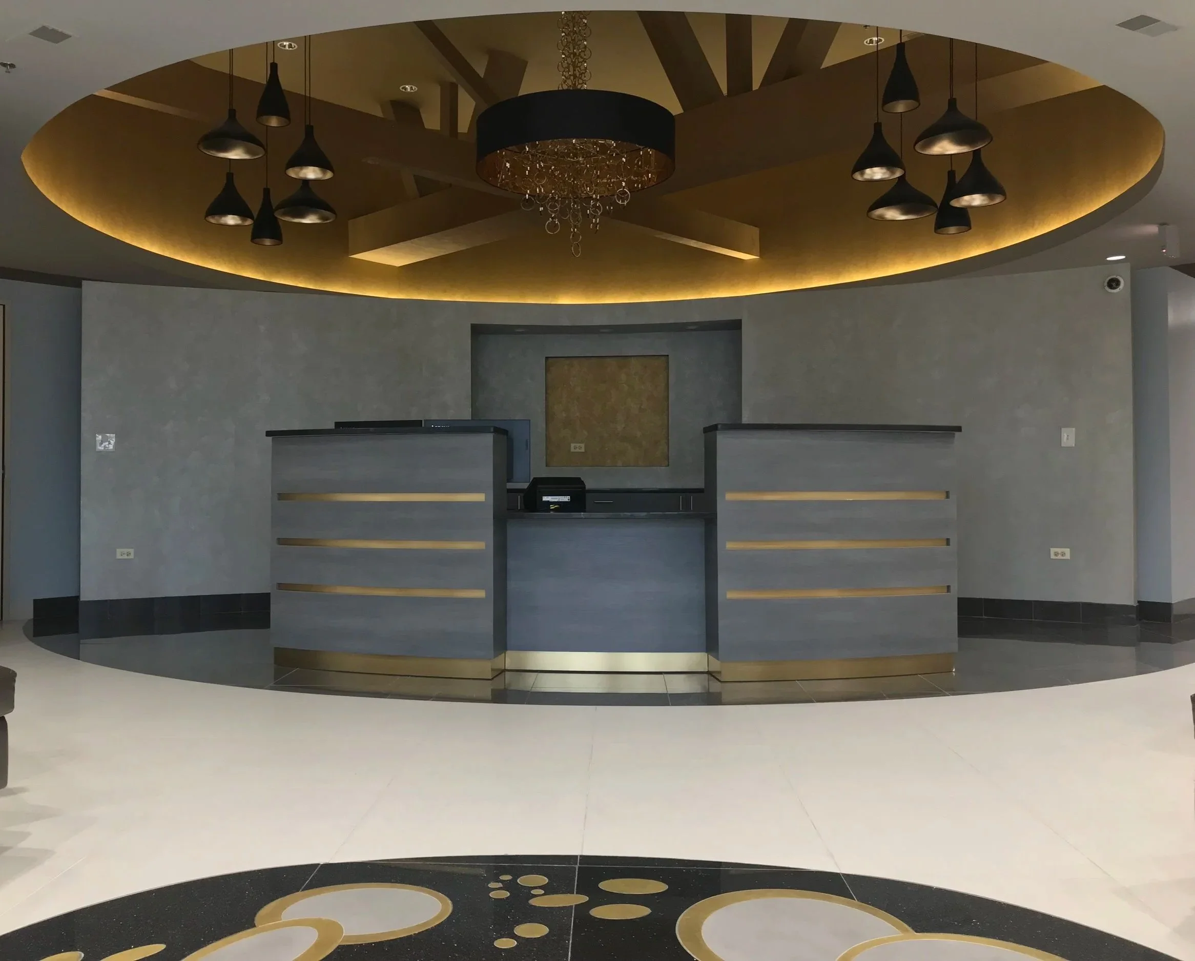 Luxury commercial lobby with circular gold ceiling, chandelier, and custom reception desks