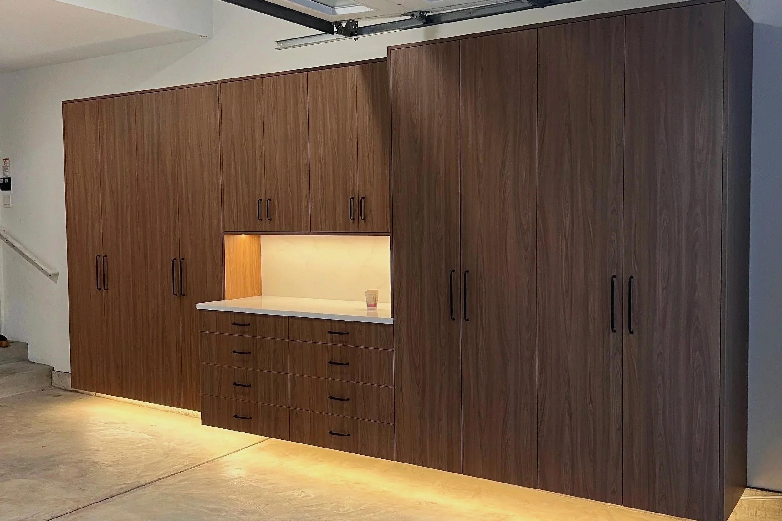 Wall-to-wall wood garage cabinets with open work alcove and LED toe-kick lighting