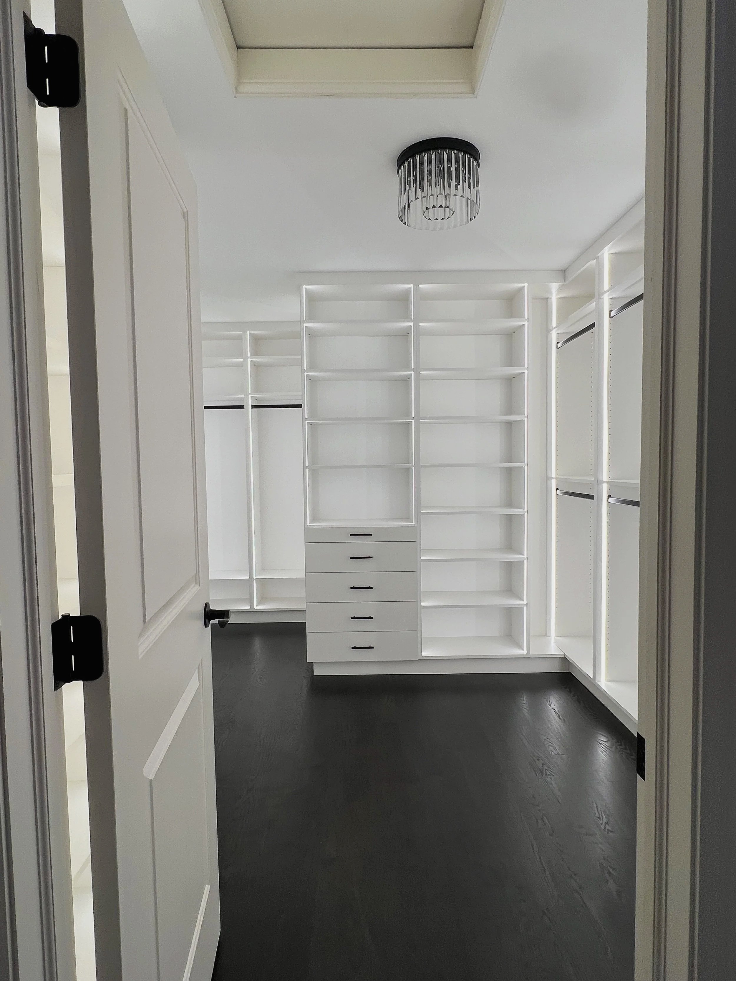 White custom walk-in closet with LED-lit shelving and dark wood floor viewed from doorway