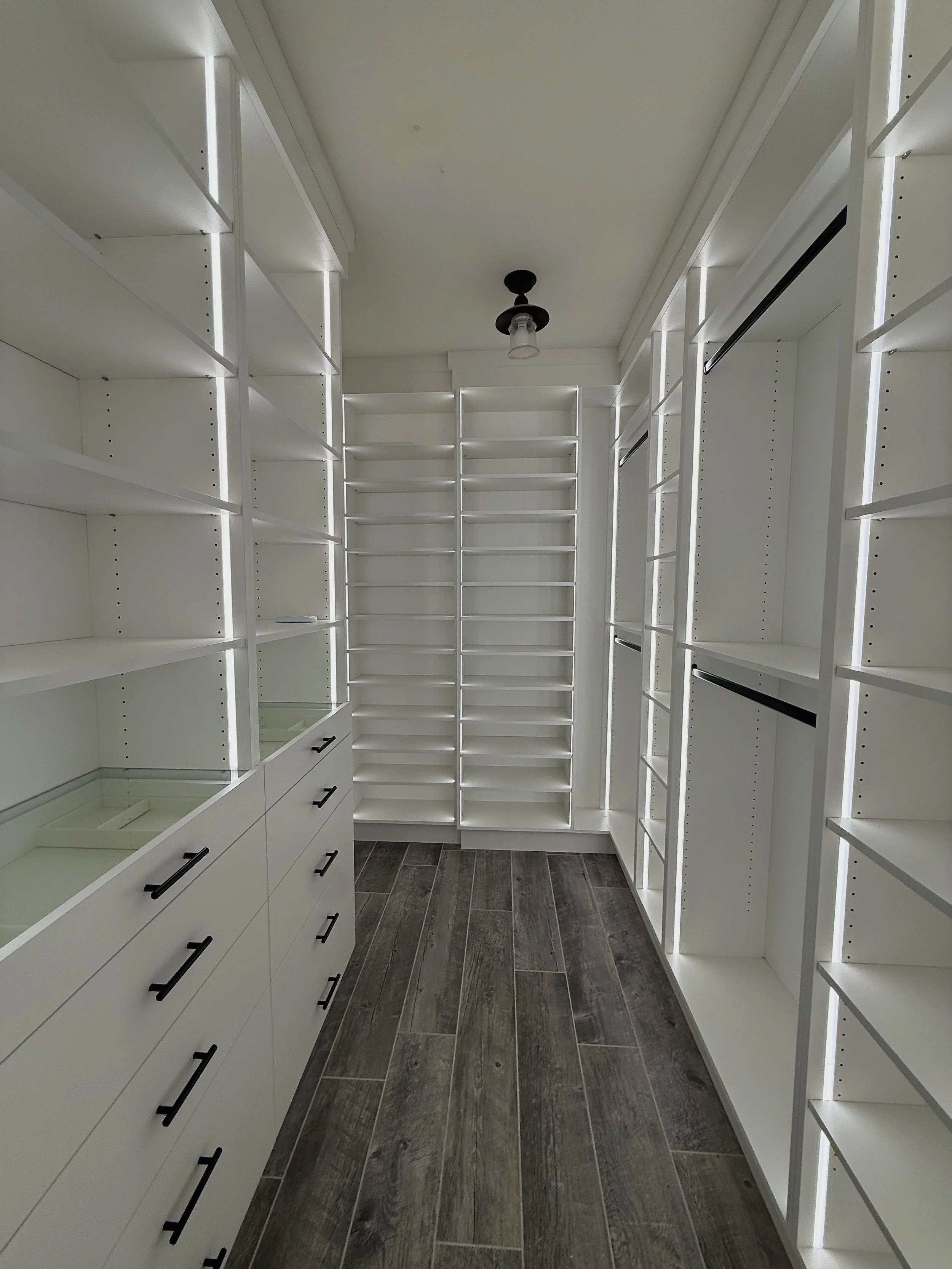 Narrow white custom walk-in closet with floor-to-ceiling shelves and hanging space