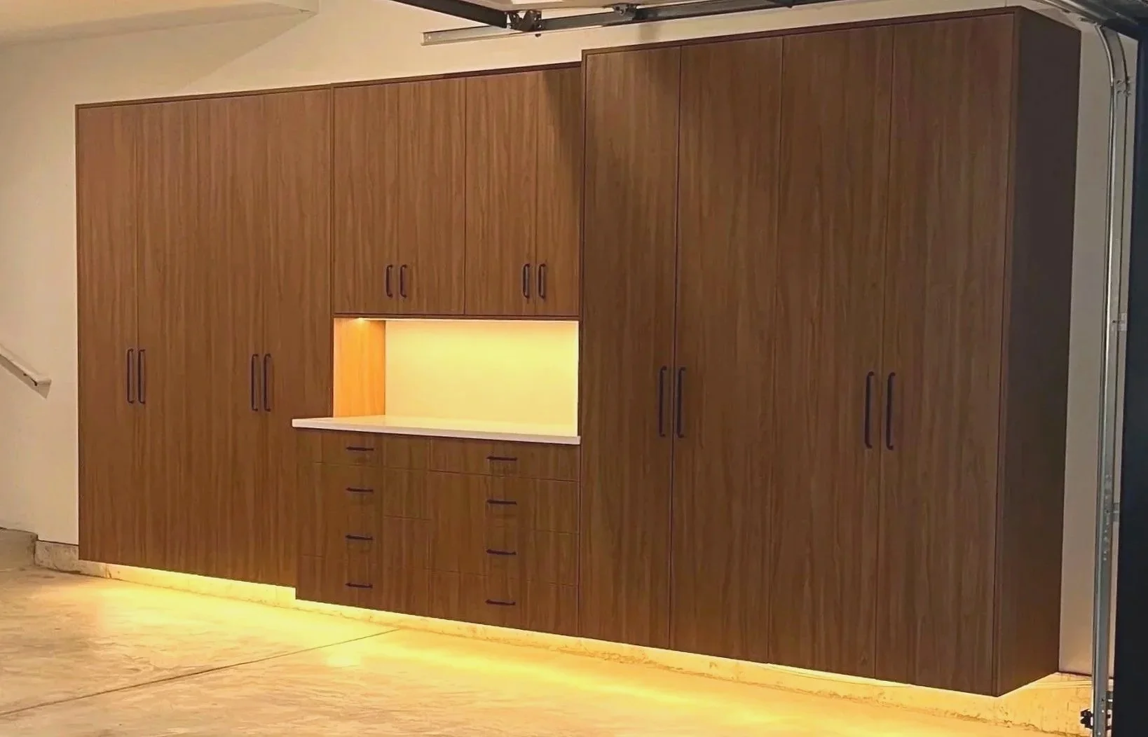 Wall-to-wall wood garage cabinets with open work alcove and LED toe-kick lighting