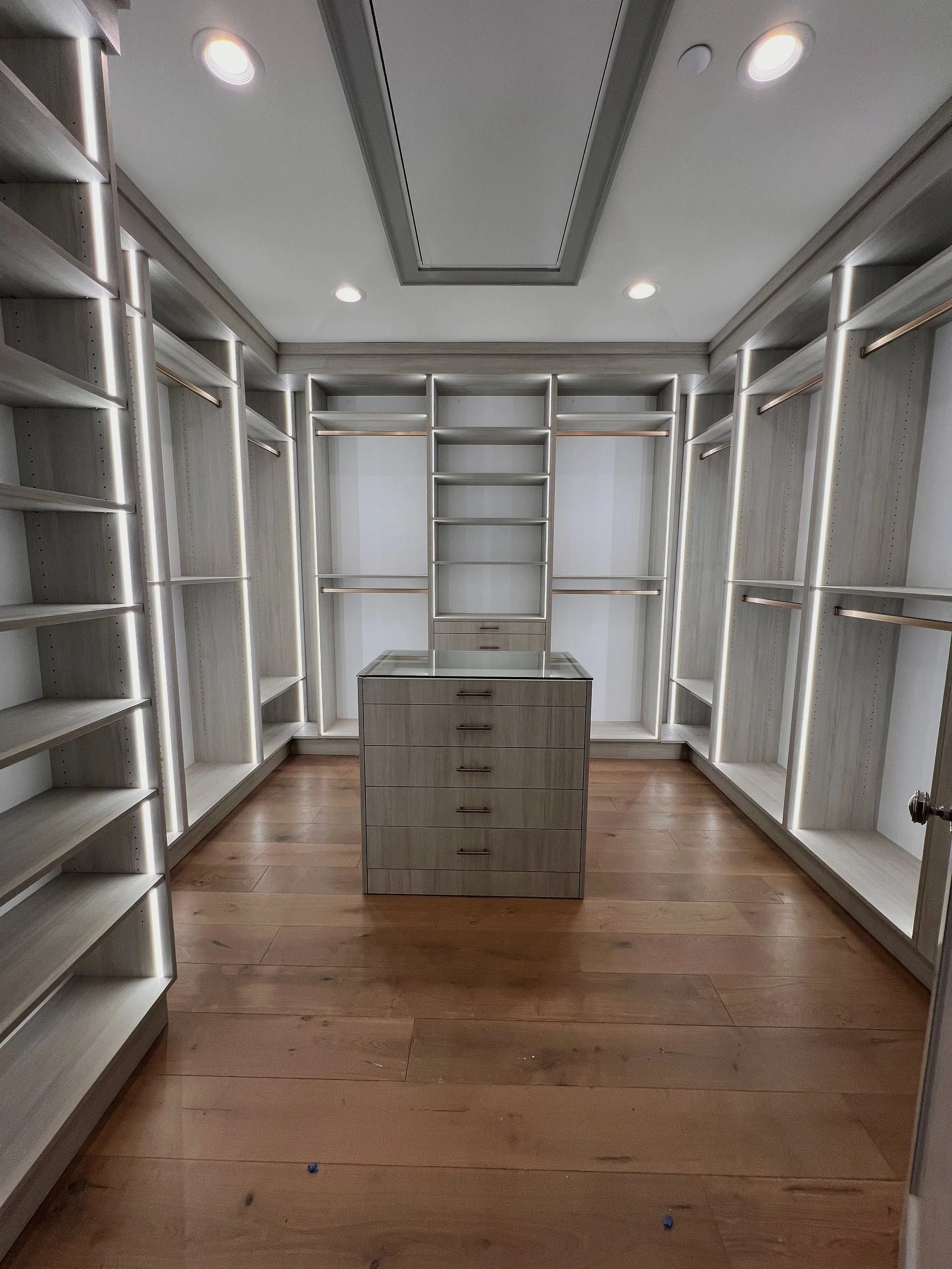 Gray custom walk-in closet with LED framed hanging sections and center storage island