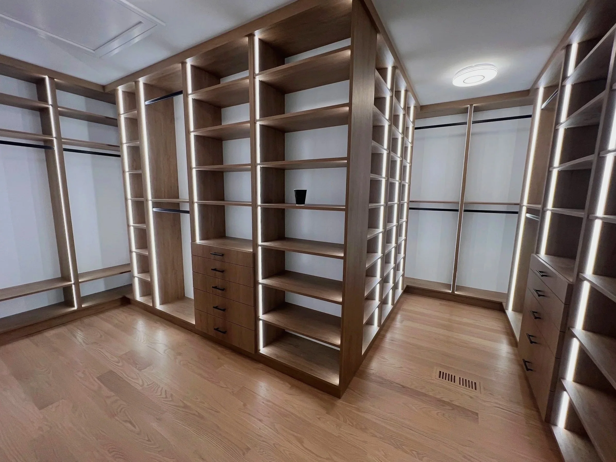 Corner wood custom walk-in closet with tall open shelves and integrated LED lighting