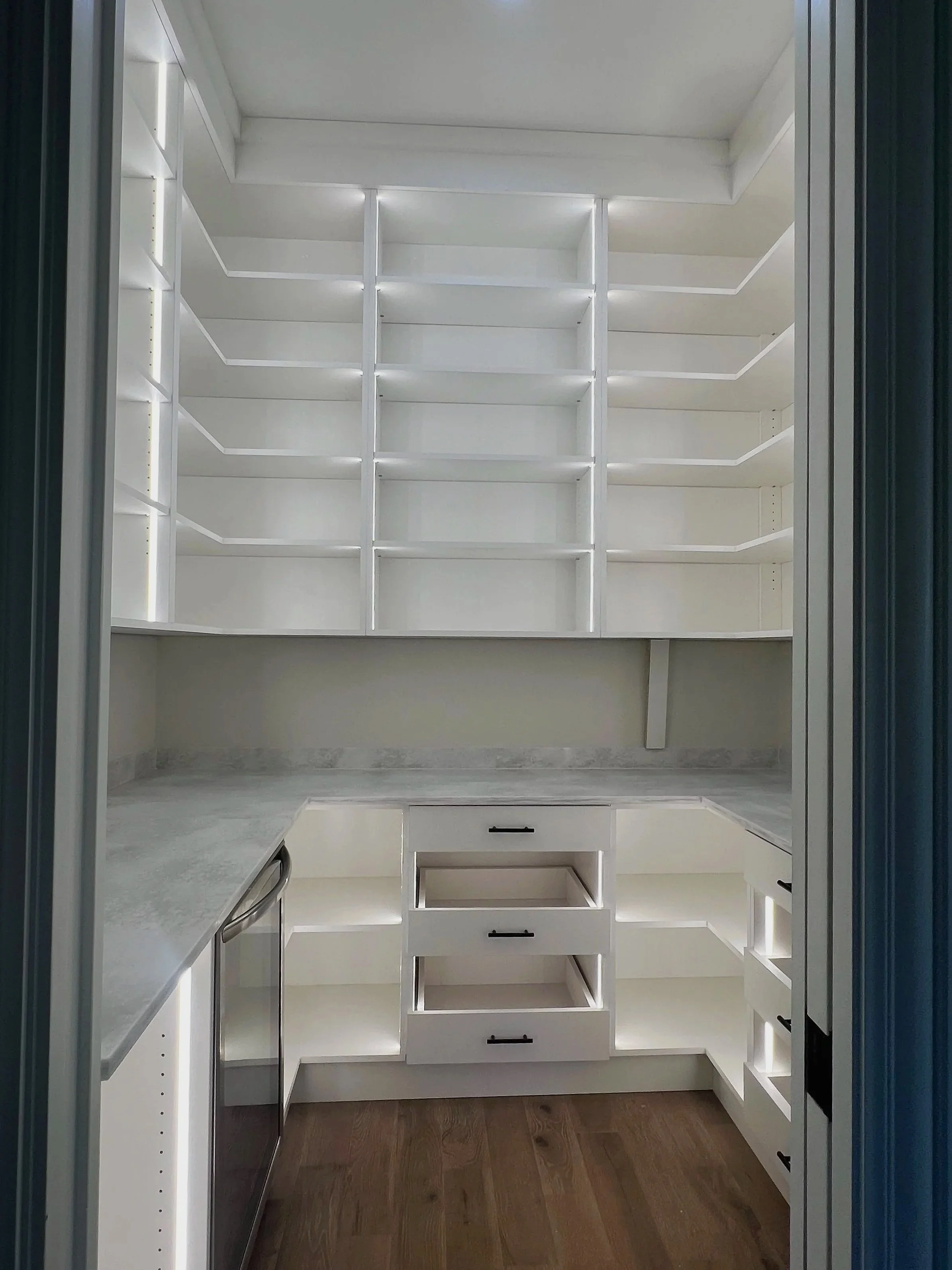 White custom pantry with L-shaped shelving, drawers, and dishwasher below counter